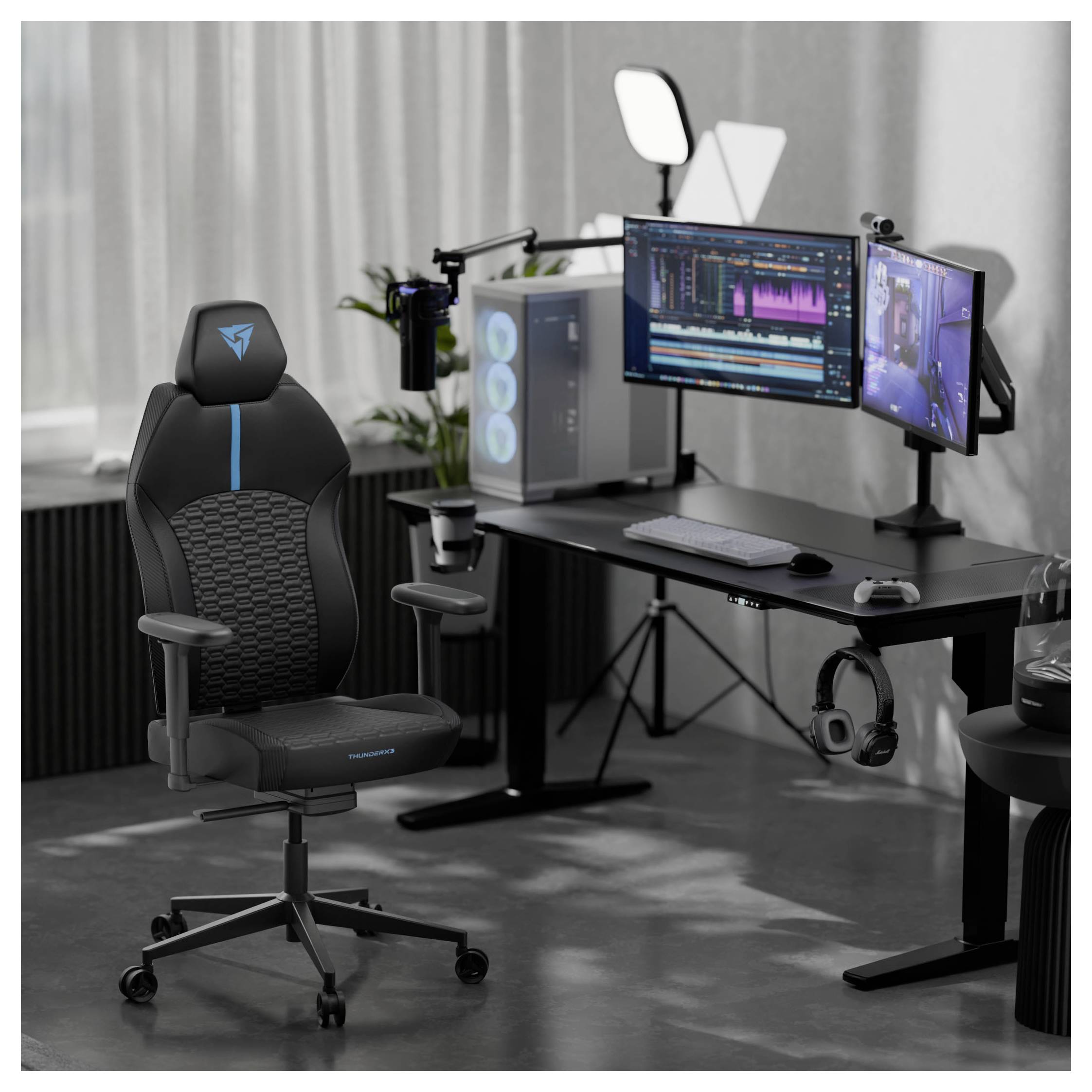 Eine Gaming-Einrichtung mit zwei Monitoren auf einem Schreibtisch, auf denen Bearbeitungssoftware gezeigt wird. Ein Gaming-Stuhl, Mikrofon und ein PC mit RGB-Beleuchtung sind vorhanden.