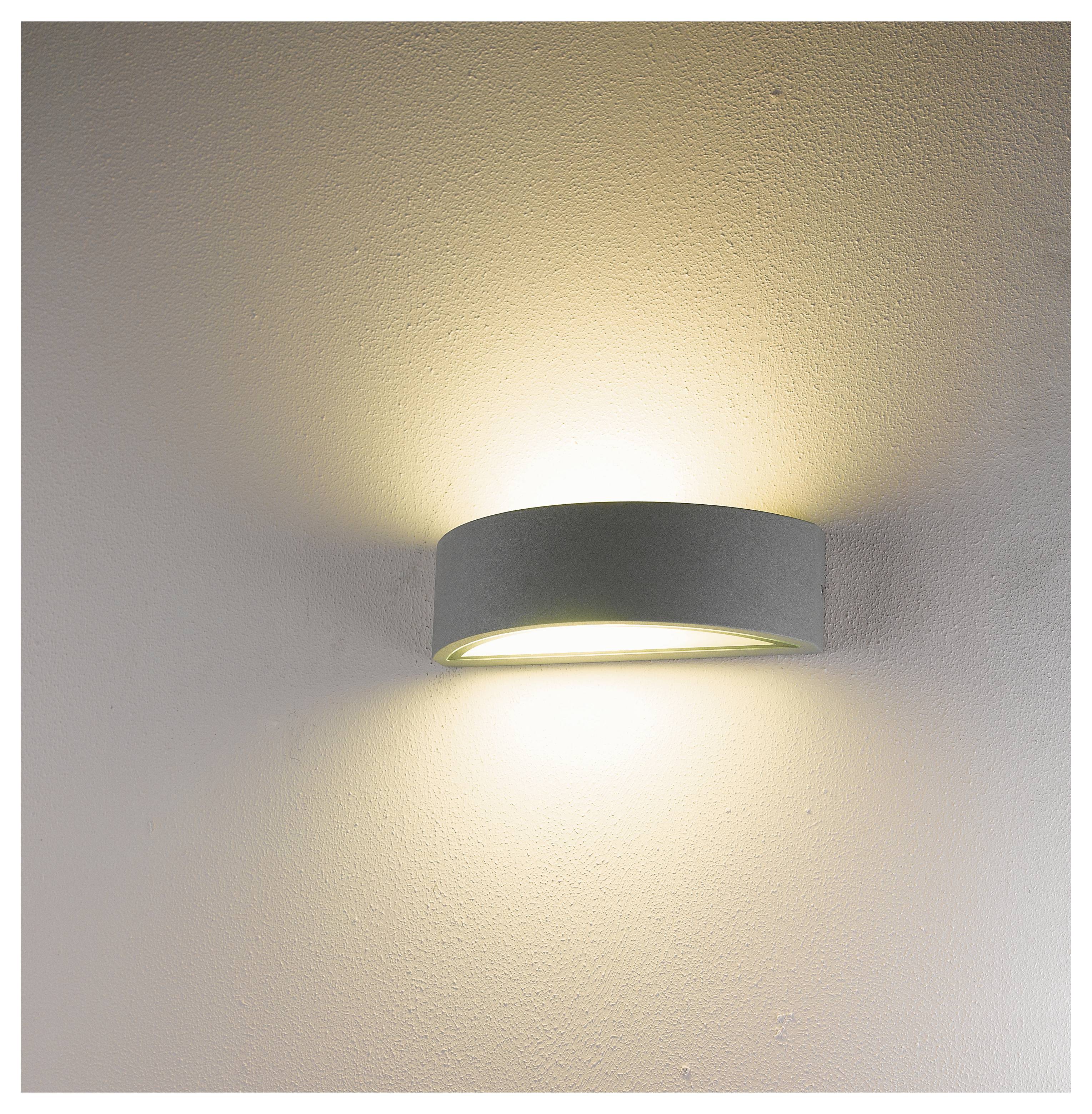 Eine moderne Wandleuchte strahlt weiches, warmes Licht auf eine weiße Wand und erzeugt einen sanften Schein, der das elegante, zylindrische Design hervorhebt.