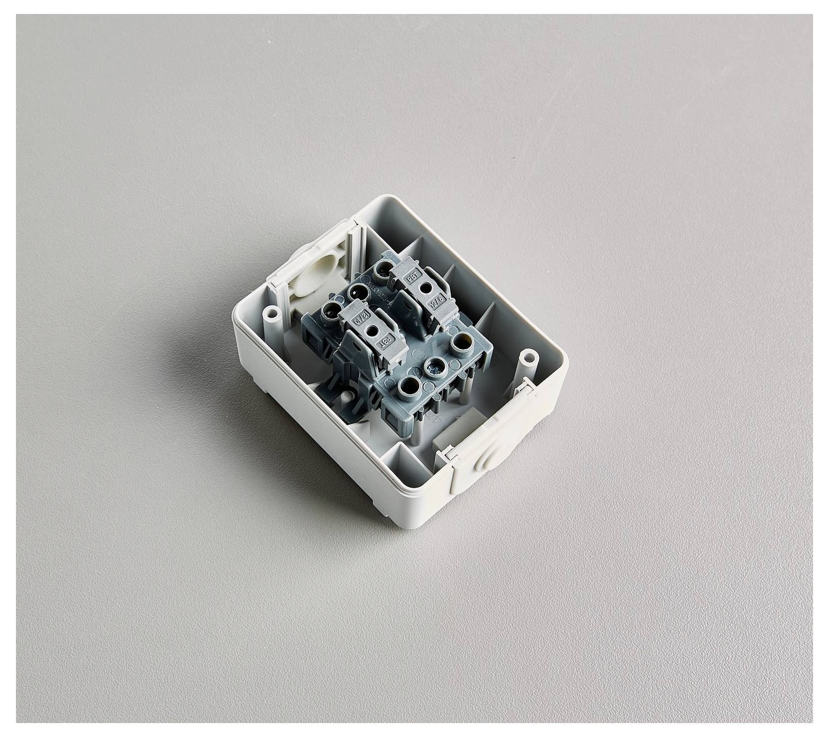 Eine offene elektrische Verteilerdose, die interne Verdrahtungsanschlüsse und Klemmen zeigt, auf einer grauen Oberfläche platziert.