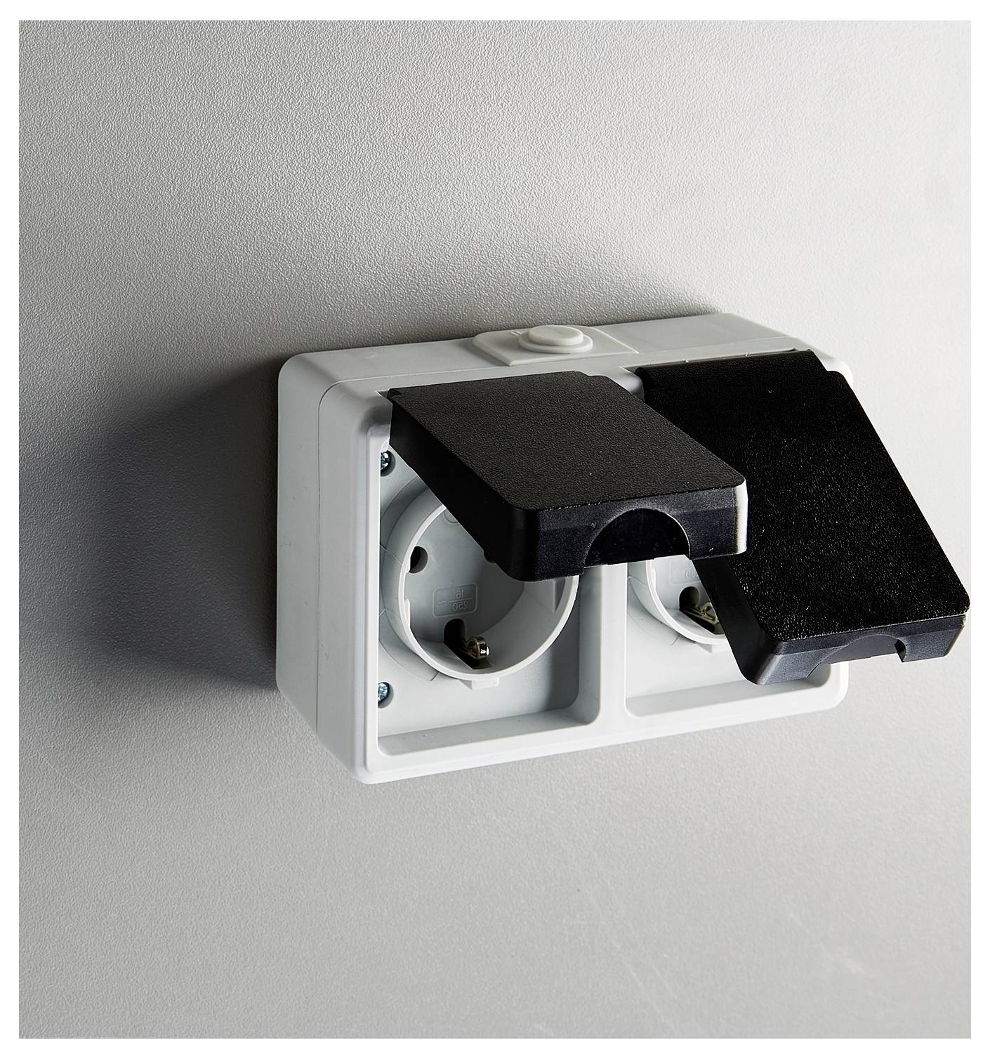 Eine doppelte Steckdose mit schwarzen Abdeckungen, an einer Wand montiert, wobei eine Abdeckung geöffnet ist und eine Steckbuchse zeigt.