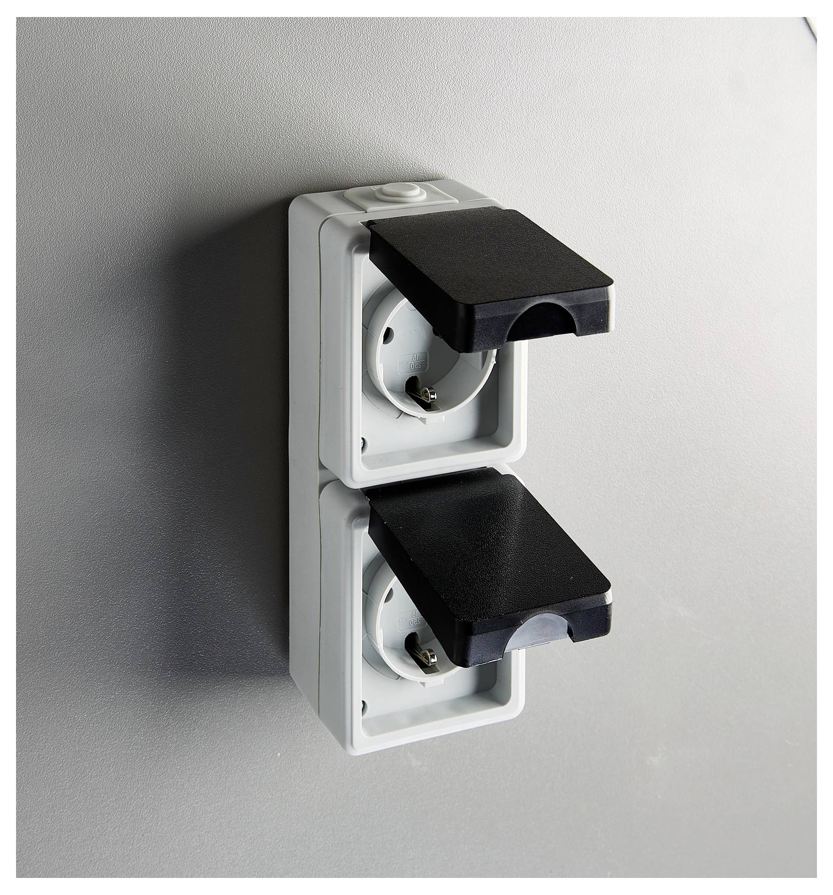 Zwei Outdoor-Stromsteckdosen mit schwarzen Schutzabdeckungen, an einer grauen Wand montiert, für Witterungsbeständigkeit konzipiert.