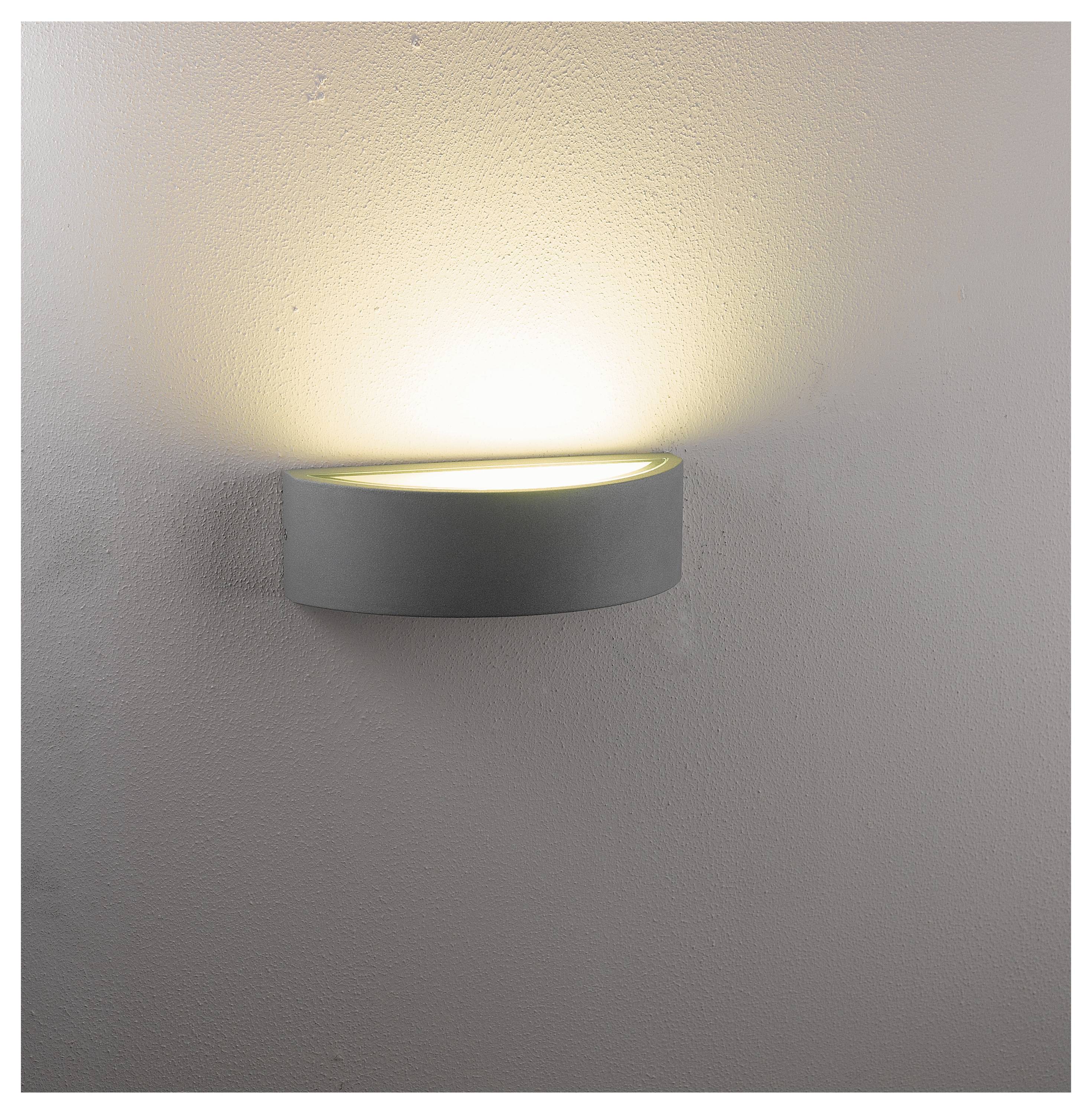 Eine wandmontierte Leuchte verbreitet ein sanftes, nach oben gerichtetes Licht und erzeugt eine warme Atmosphäre vor dem neutralfarbenen Wandhintergrund.