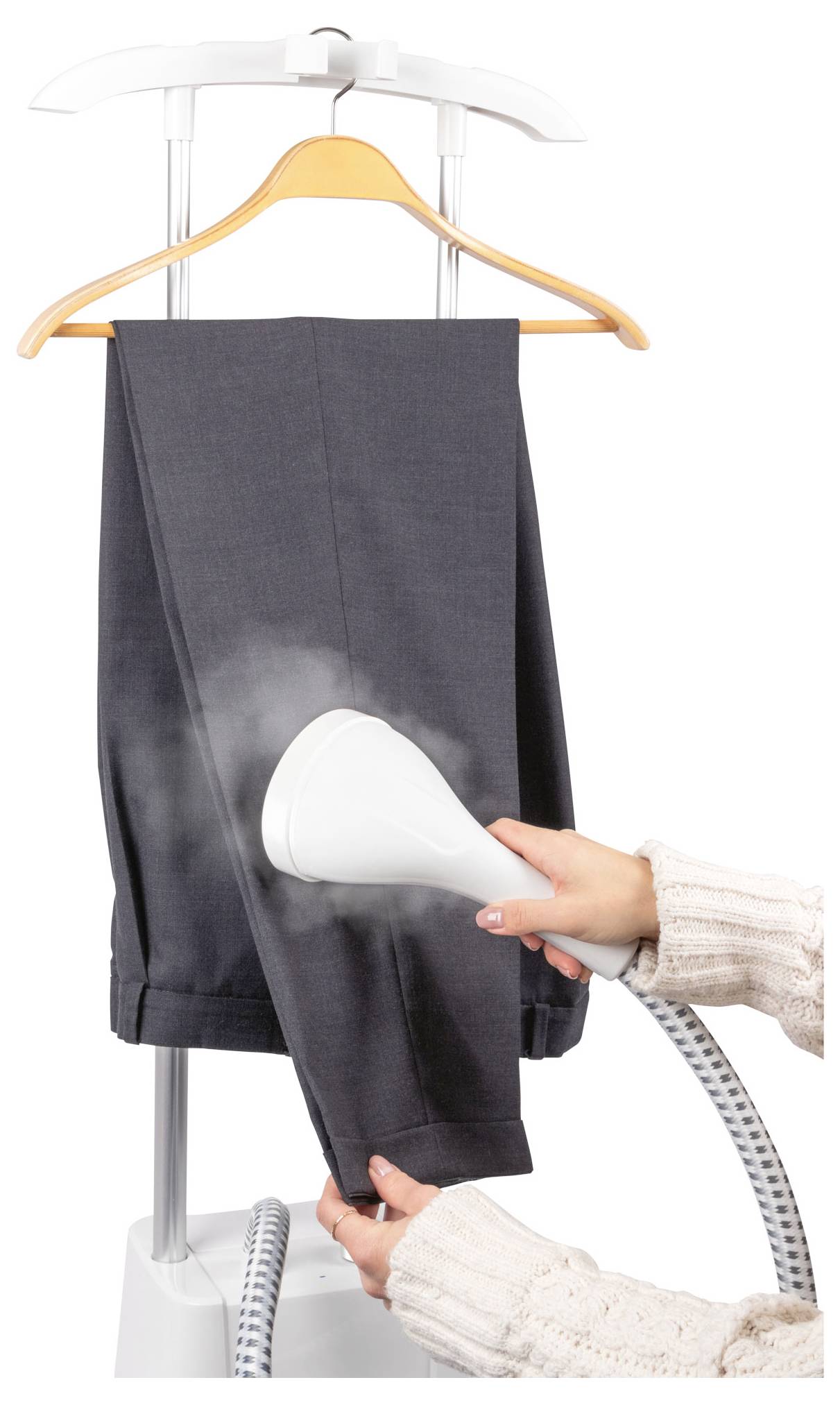 Eine Person dampft eine graue Hose, die an einem Holzbügel hängt, mit einem weißen Dampfbügler und entfernt Falten.