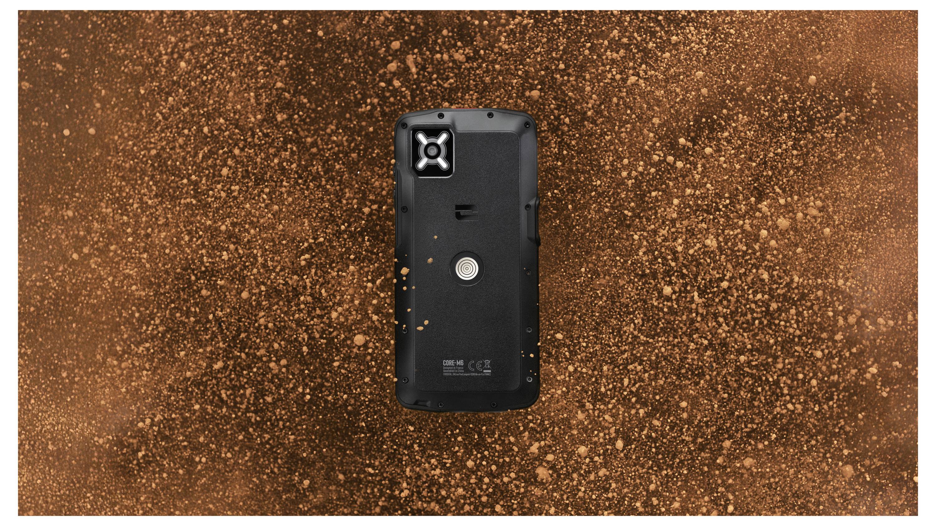 Ein robustes schwarzes Smartphone mit strukturierter Rückseite, zentriert vor einem dynamischen, wirbelnden braunen und orangefarbenen Staubbild.