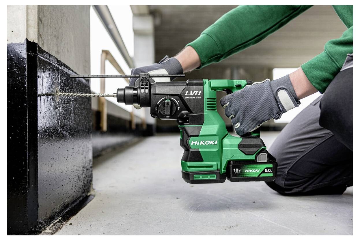 Eine Person mit grauen Handschuhen verwendet einen grün-schwarzen Bohrer, um ein Loch in eine schwarze Metalloberfläche zu bohren, was auf eine Bauaktivität hinweist.