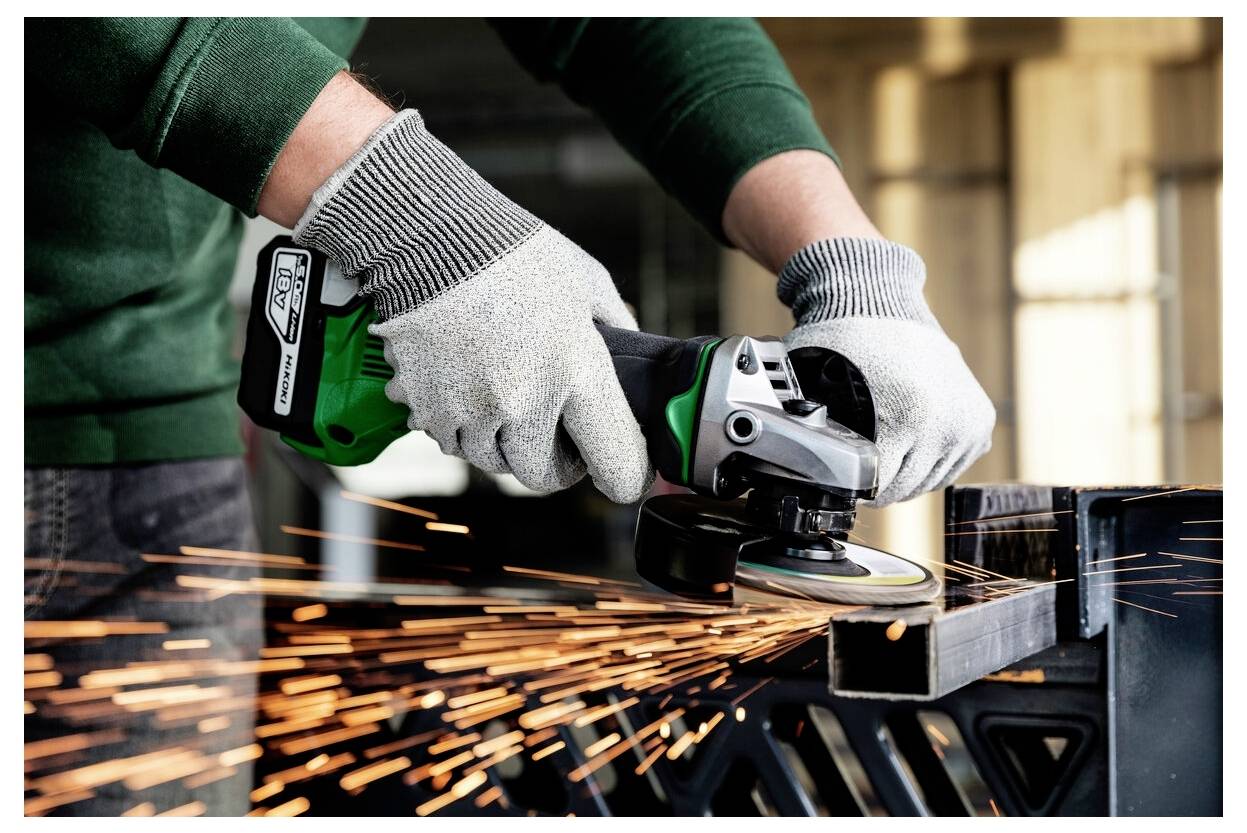 Eine Person mit Handschuhen bedient einen Winkelschleifer und erzeugt helle Funken, während sie ein Metallbauteil zerschneidet.
