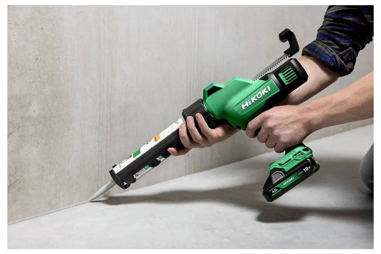 Eine Person verwendet eine grüne kabellose HiKOKI-Kartuschenpistole, um Dichtungsmasse entlang einer Betonnaht aufzutragen.