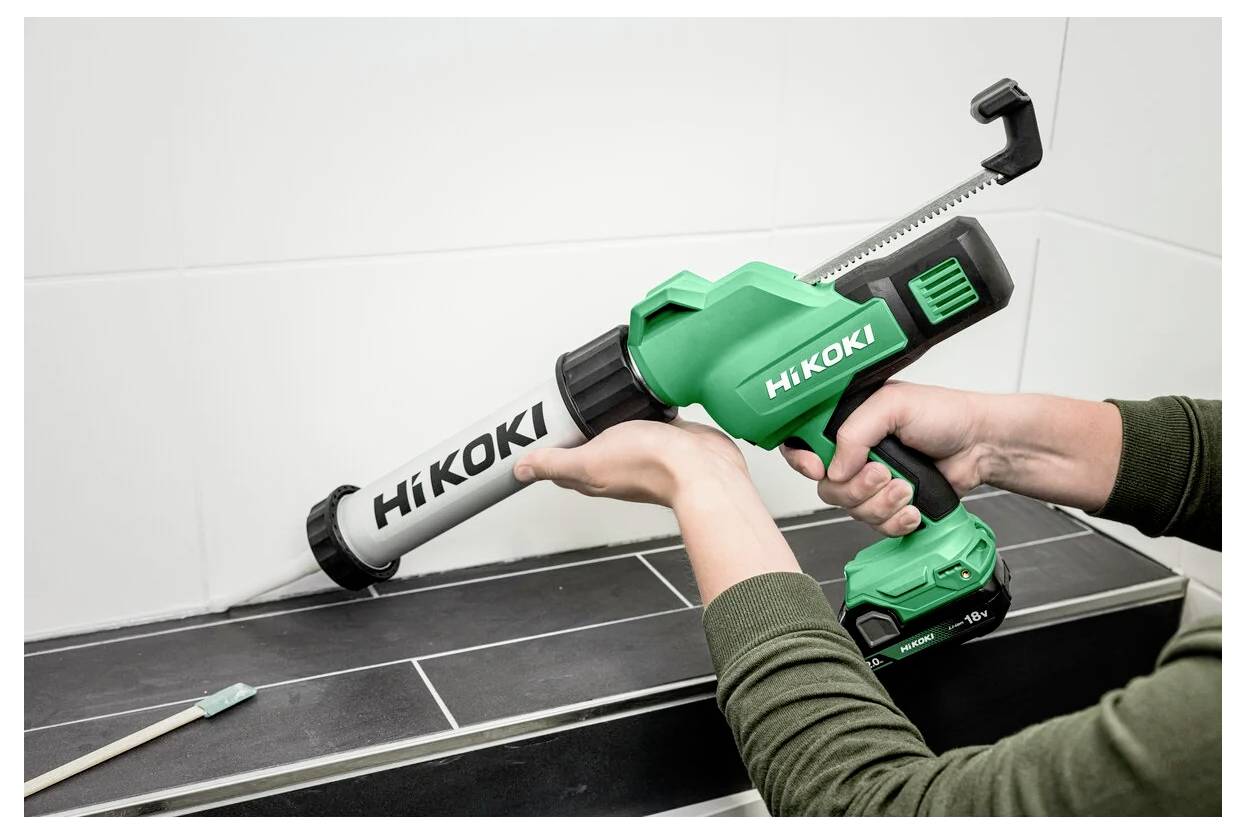 Eine Person verwendet eine grüne HiKOKI kabellose Kartuschenpistole, um Dichtstoff entlang der Kante einer gefliesten Oberfläche aufzutragen.