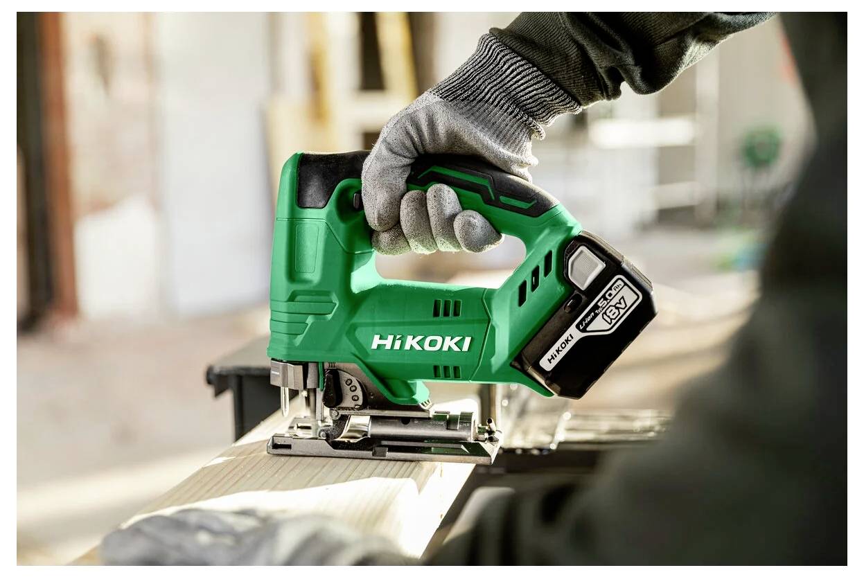 Eine Person, die mit einer HiKOKI Akku-Stichsäge Holz auf einer Werkbank schneidet und dabei Schutzhandschuhe in einer Werkstattumgebung trägt.