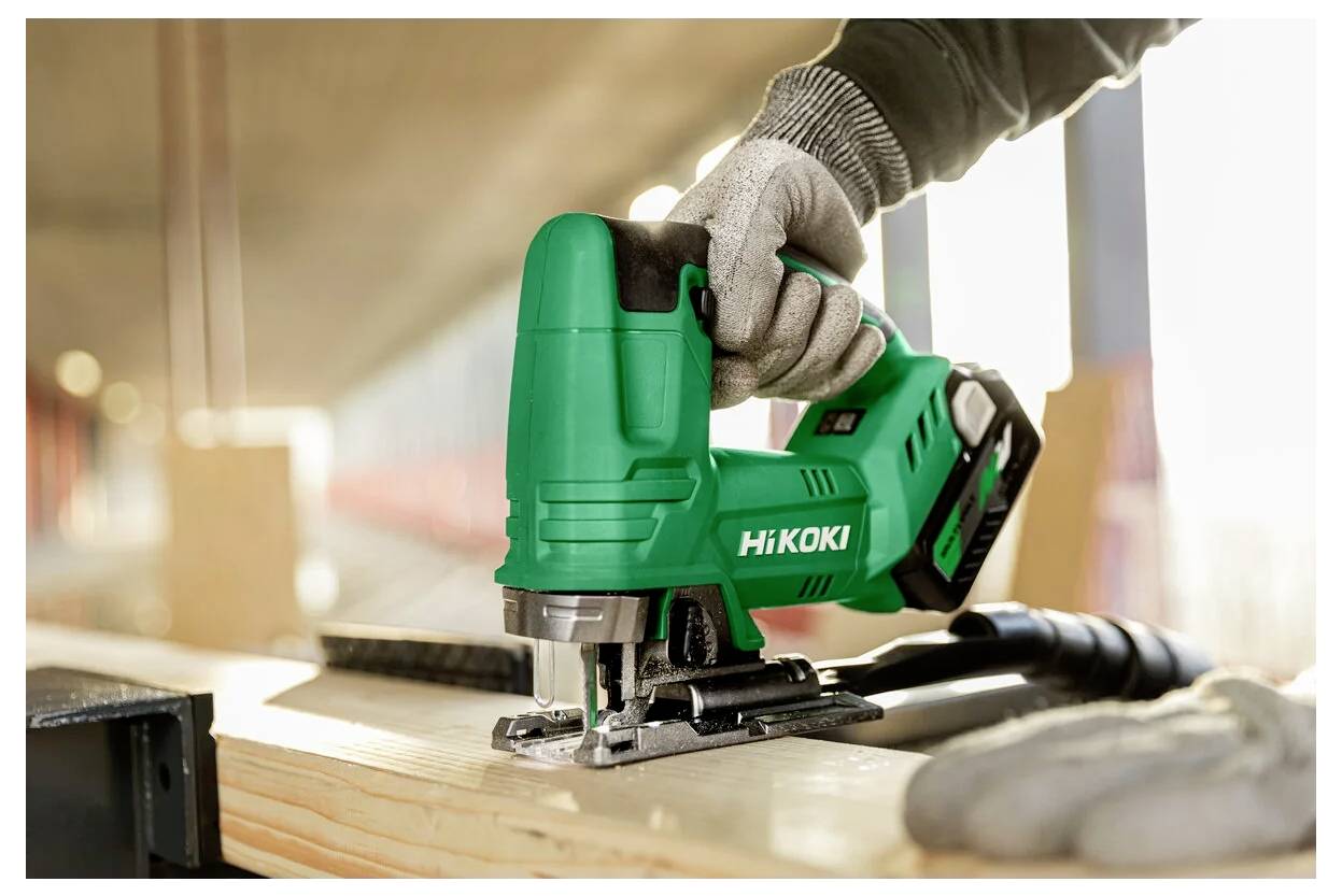 Eine Person mit Arbeitshandschuhen verwendet eine grüne HiKOKI-Stichsäge, um ein Holzstück auf einer Baustelle zu schneiden.