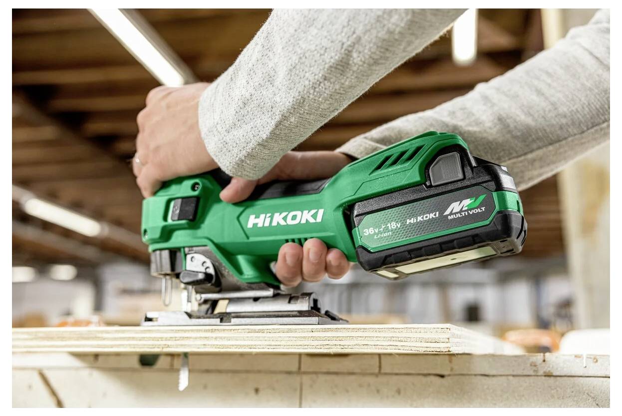 Eine Person verwendet ein grünes HiKOKI kabelloses Werkzeug, um eine Holzplatte in einer Werkstatt zu schneiden und zeigt dabei die Funktionalität und Benutzerfreundlichkeit des Geräts.