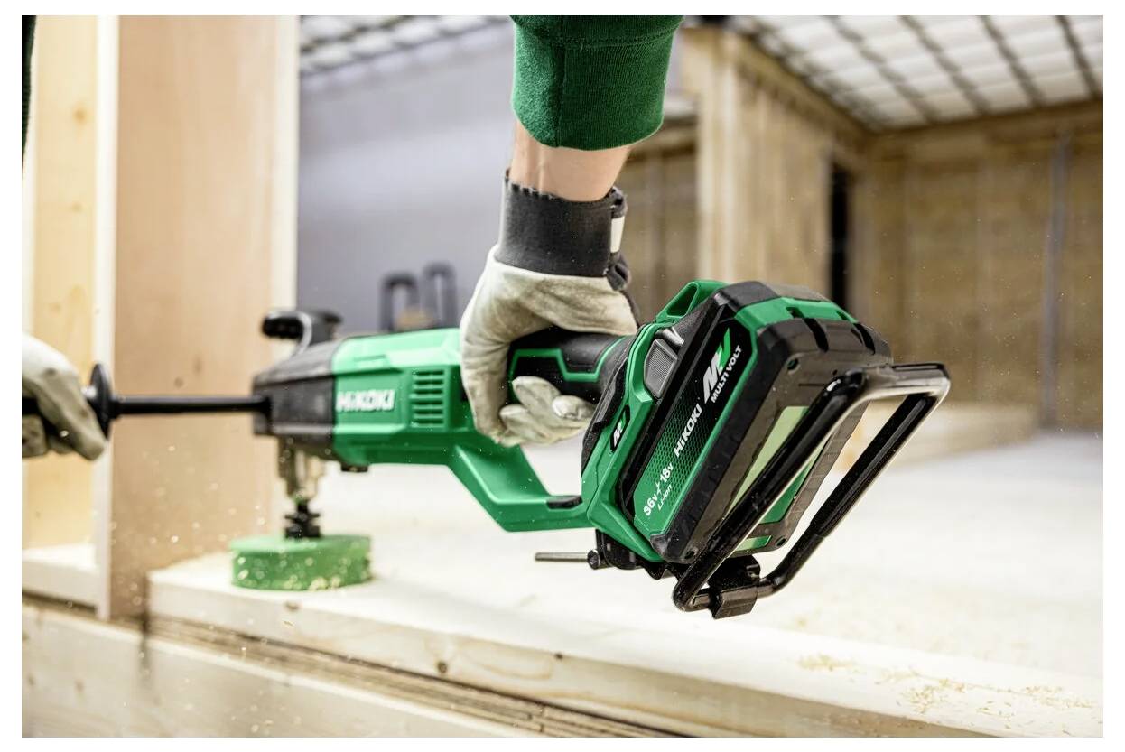 Eine Person verwendet eine grüne elektrische Säbelsäge, um ein Holzstück drinnen zu zersägen. Holzspäne sind sichtbar, und die Säge ist angeschlossen.