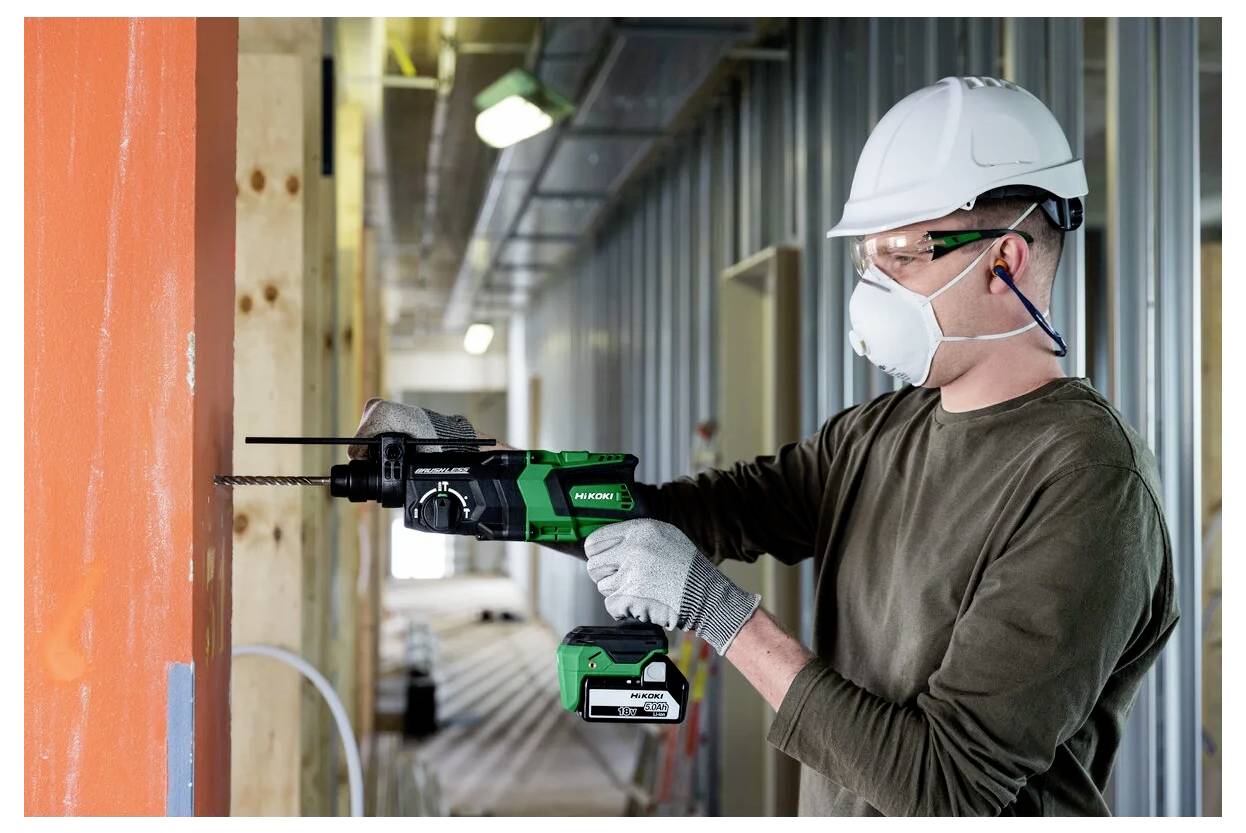 Ein Bauarbeiter mit Sicherheitsausrüstung verwendet einen Akkuschrauber an einem Holzbalken in einem im Bau befindlichen Gebäude.