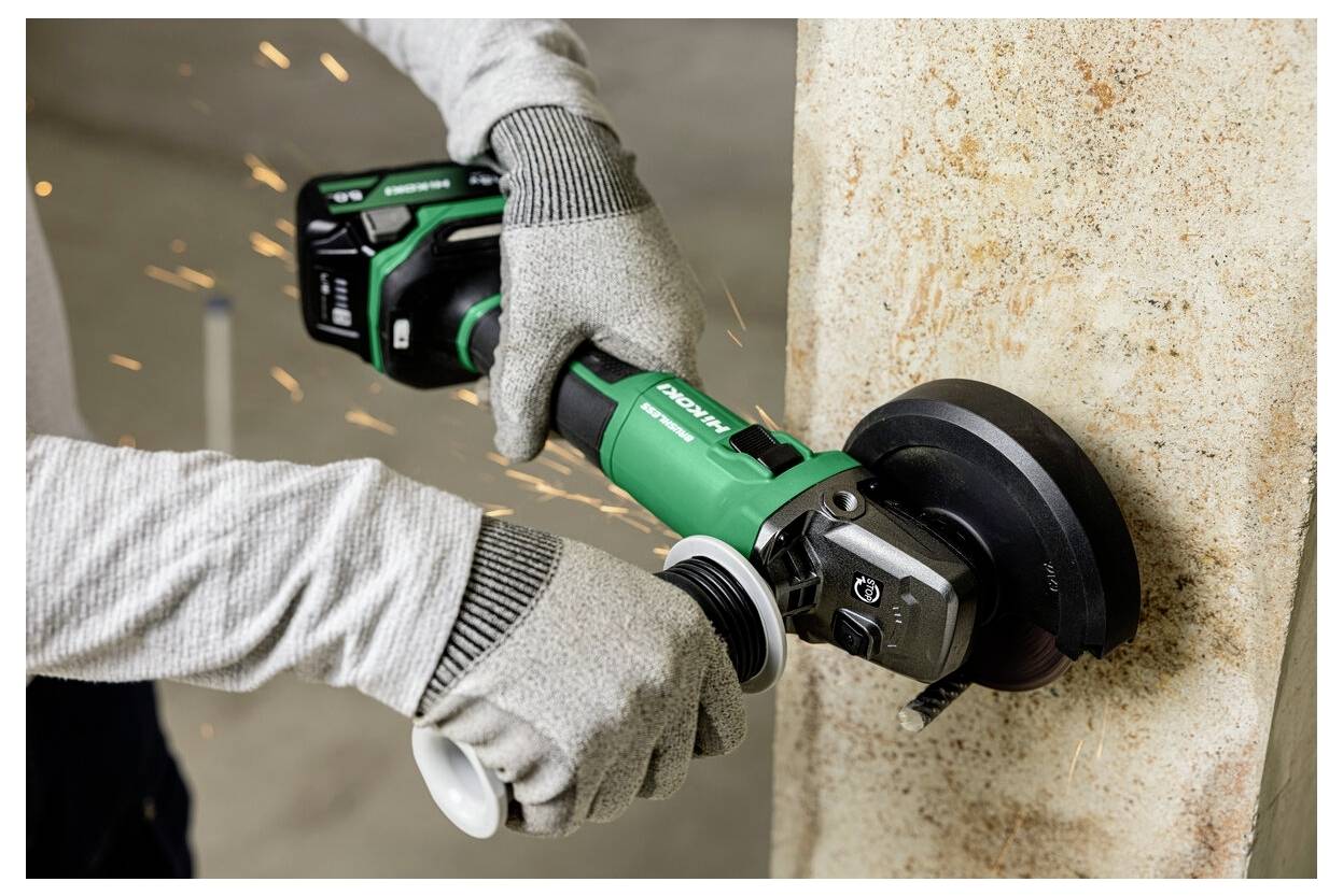 Eine Person mit Schutzhandschuhen verwendet einen elektrischen Winkelschleifer, um in eine Betonwand zu schneiden, wobei beim Betrieb des Werkzeugs Funken entstehen.