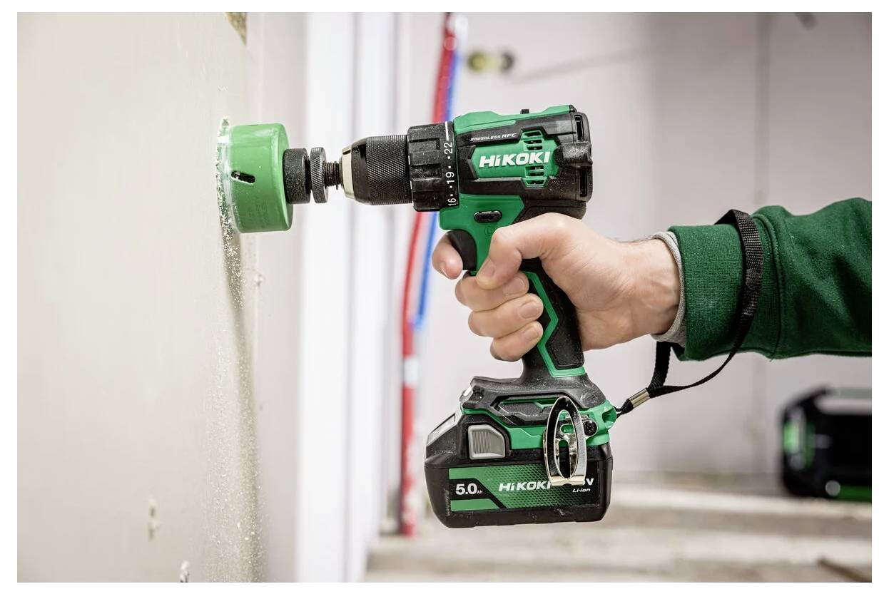 Eine Person verwendet einen grünen kabellosen Akkuschrauber, um ein Loch in eine Wand im Innenraum zu bohren.