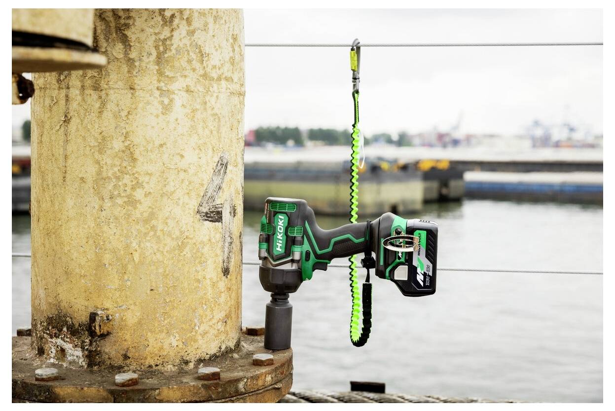 Ein grünes und schwarzes Elektrowerkzeug, das mit einer Sicherheitsleine an einer gelben Säule befestigt ist, in der Nähe eines Wassers mit industrieller Hintergrundkulisse.