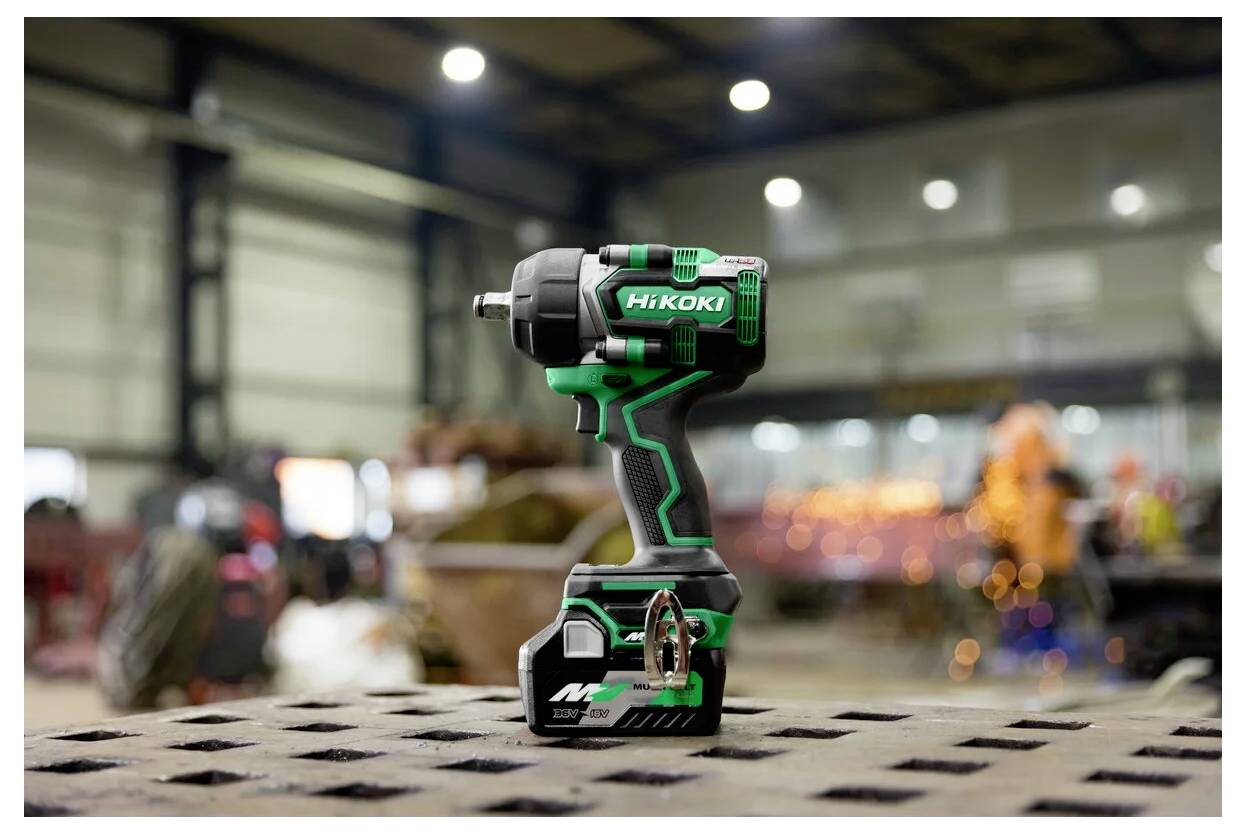 Eine grüne und schwarze kabellose Arbeitsmaschine mit einer Markenetikette, die auf einer gelochten Metalloberfläche in einer industriellen Werkstattumgebung platziert ist.