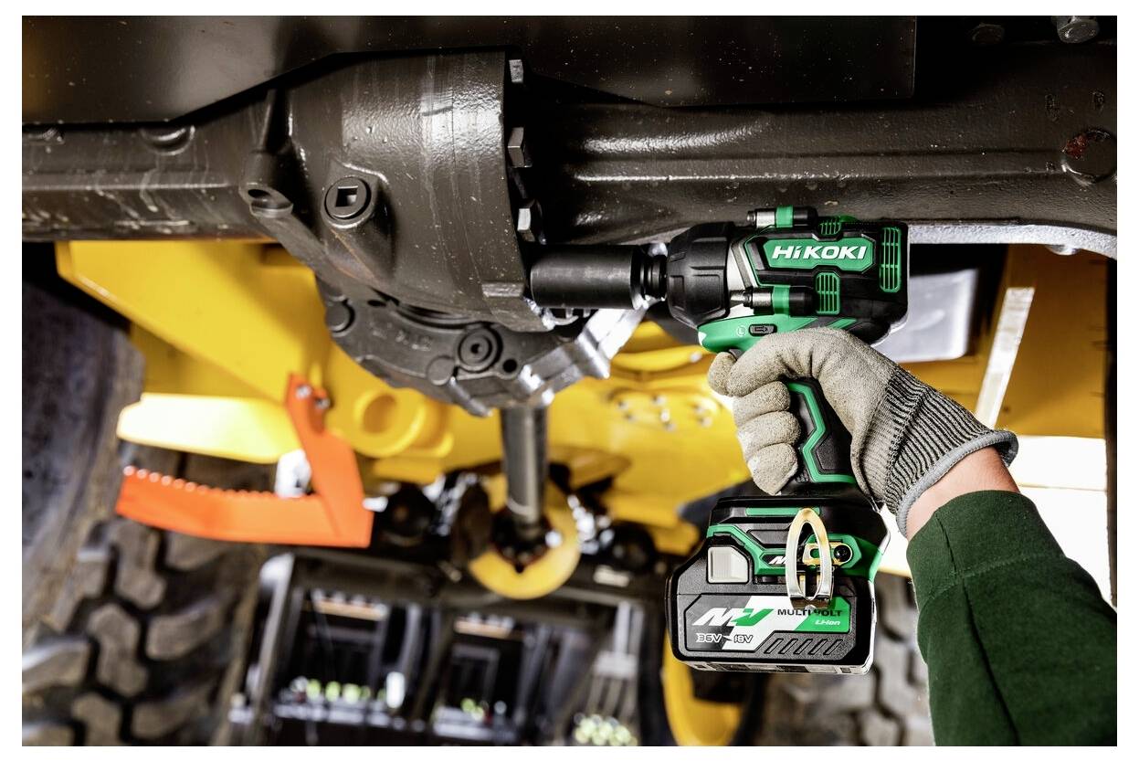 Eine Person verwendet einen grünen und schwarzen HiKOKI Akku-Schlagschrauber, um eine Schraube unter einer Baumaschine anzuziehen.