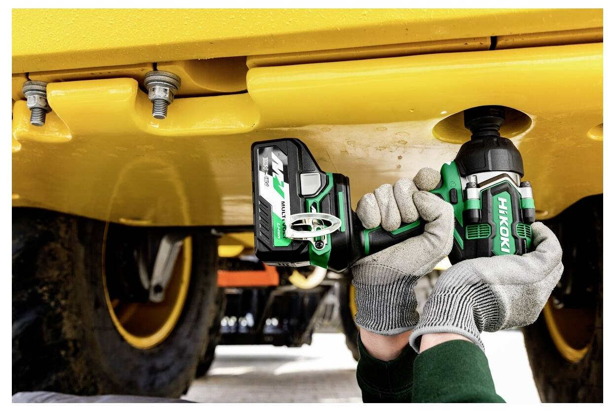 Eine Person verwendet ein grün-schwarzes Werkzeug, um eine Schraube unter schwerer Maschine zu befestigen und trägt dabei Schutzhandschuhe.