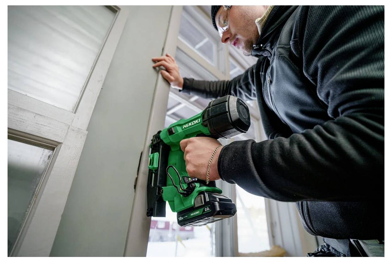Eine Person verwendet einen grünen, kabellosen Akkuschrauber, um einen Türrahmen im Innenbereich zu installieren. Sie wirkt konzentriert und trägt eine Jacke.