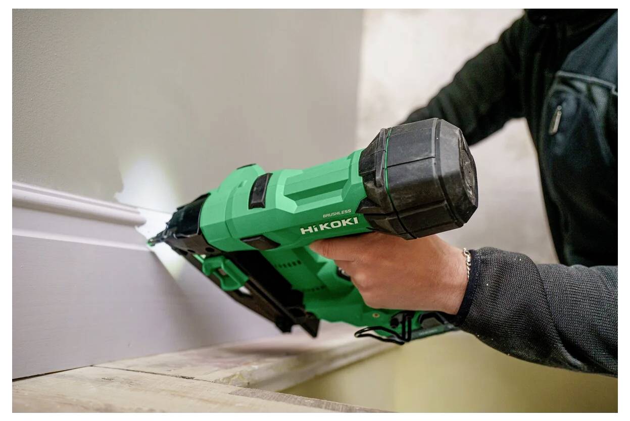 Eine Person, die einen grünen Nagelpistole verwendet, um Sockelleisten an eine Wand zu befestigen und dabei eine Heimwerkeraktivität demonstriert.