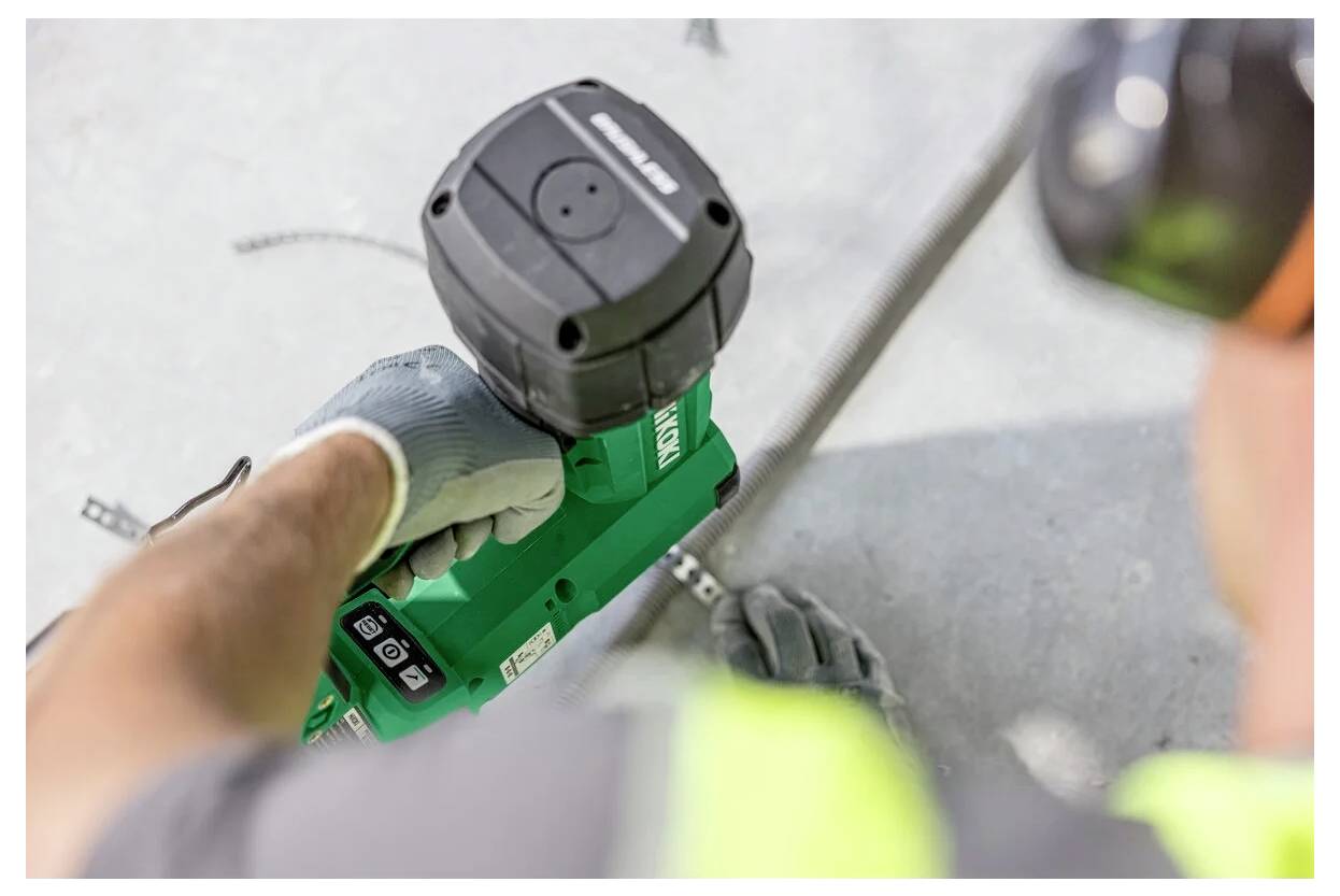 Person mit einer grünen Elektrowerkzeug auf Beton; Fokus auf den Arm mit Handschuh, der die Einstellungen anpasst.