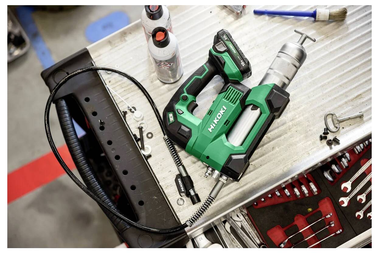 Ein grünes Elektrowerkzeug mit 'Hikoki' Branding liegt auf einer Metallwerkbank neben verschiedenen Werkzeugen und Flaschen in einer Werkstattumgebung.