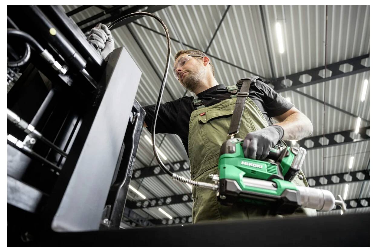 Ein Arbeiter in Arbeitskleidung und Handschuhen bedient Maschinen in einer industriellen Anlage und verwendet ein Elektrowerkzeug, um Wartungs- oder Reparaturarbeiten durchzuführen.