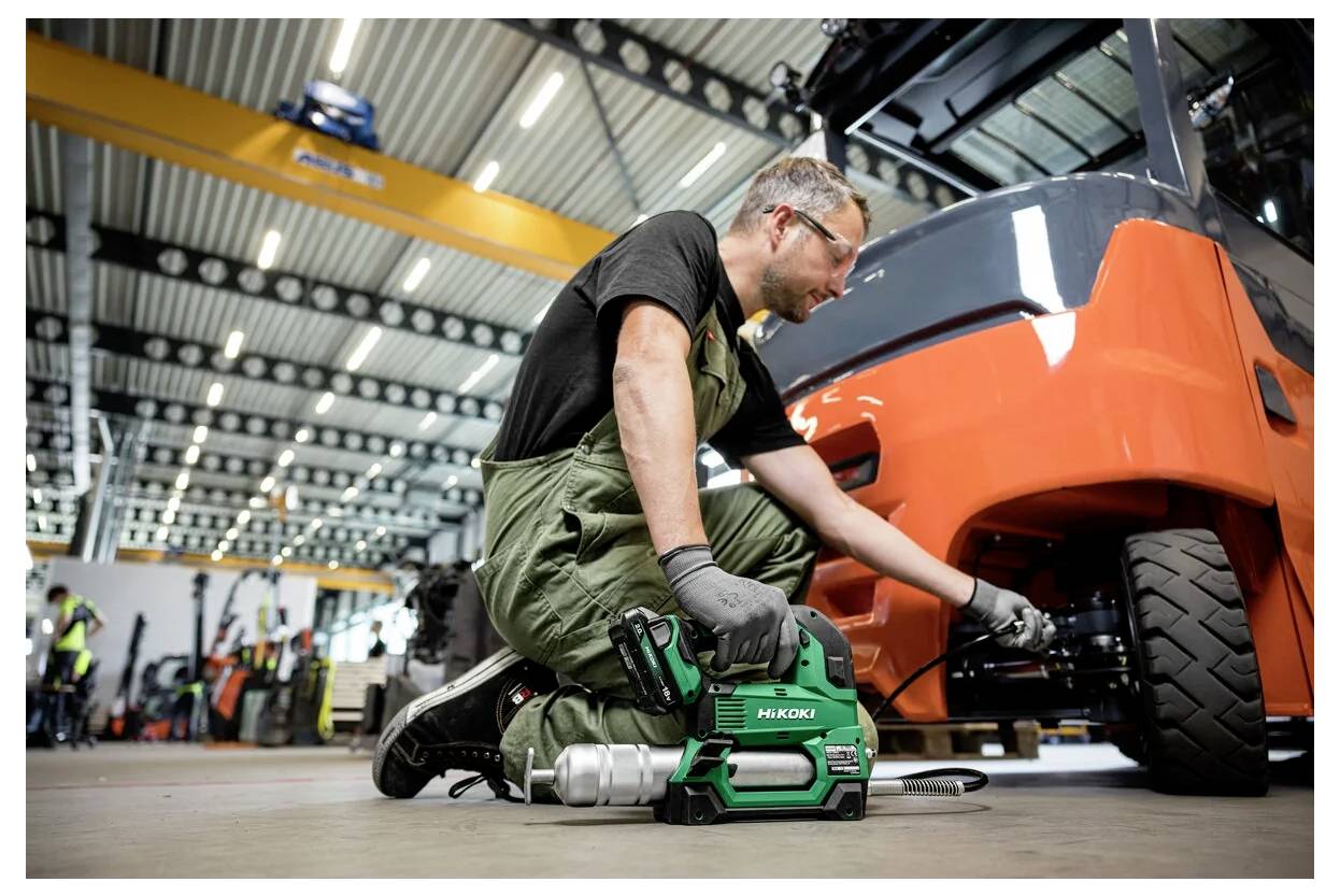 Ein Mechaniker in einer Werkstatt benutzt ein Werkzeug an einem Gabelstapler, umgeben von industrieller Ausrüstung. Die Umgebung deutet auf Fahrzeugwartung oder -reparatur hin.