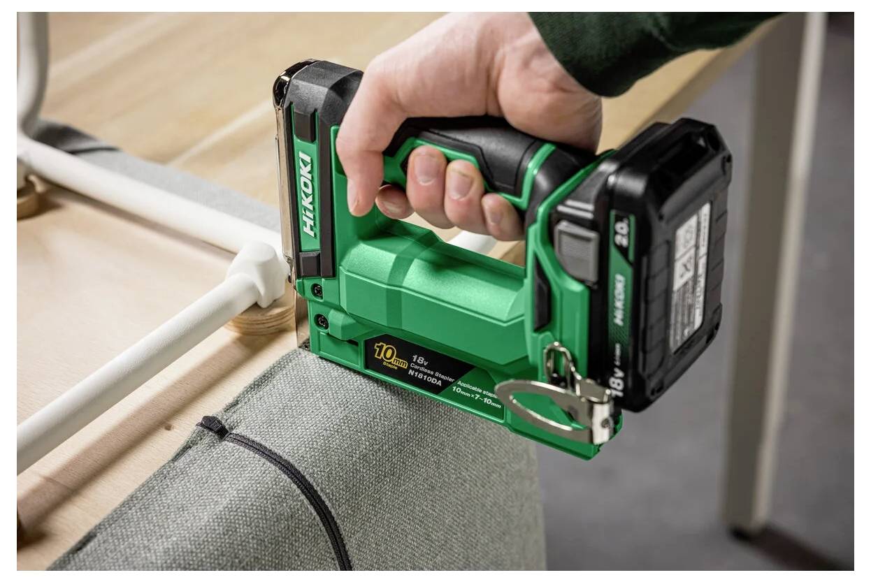 Eine Person verwendet einen grünen Hikoki-Akku-Tacker, um Stoff an einem Holzrahmen auf einem Tisch zu befestigen.