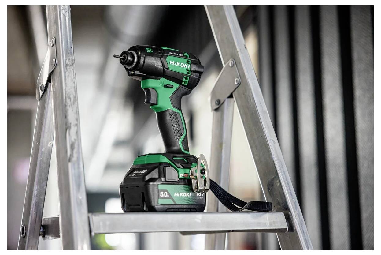 Eine grüne und schwarze kabellose Bohrmaschine mit der Aufschrift 'HiKOKI' liegt auf einer silbernen Leiter und deutet auf eine Umgebung für Bau- oder Heimwerkerarbeiten hin.