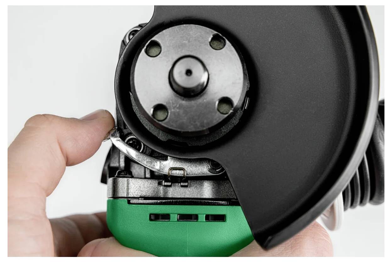 Eine Person hält einen grün-schwarzen Winkelschleifer und konzentriert sich in einer Nahaufnahme auf die Scheibe und den Sicherheitsschutz.