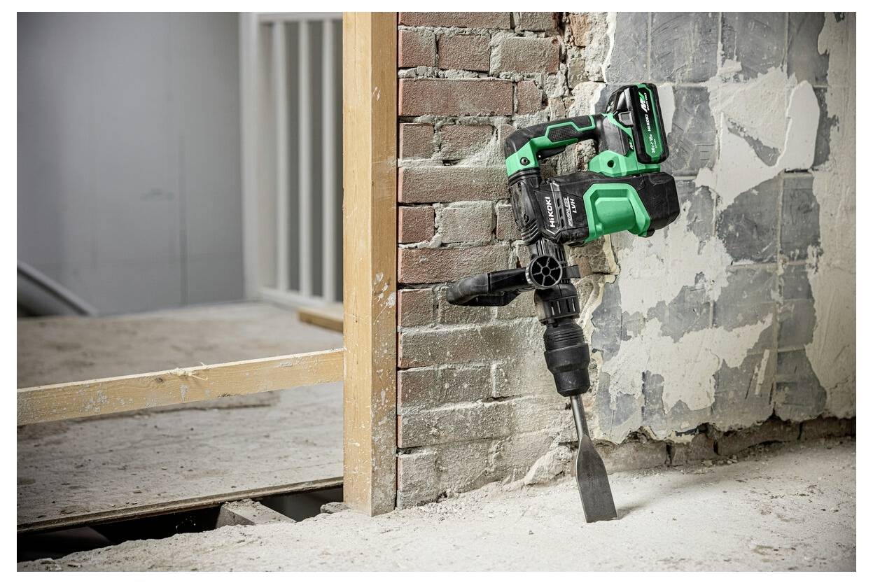 Ein grüner und schwarzer Abbruchhammer lehnt an einer teilweise demolierten Mauer aus Ziegeln und Putz in einem Raum, der renoviert wird.