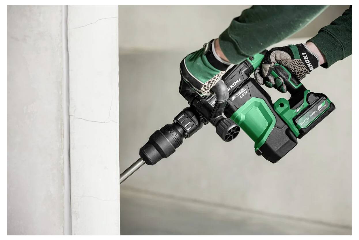 Eine Person mit Handschuhen verwendet einen grün-schwarzen kabellosen Akkuschrauber, um an einer Betonoberfläche zu arbeiten und konzentriert sich dabei auf den Metallbohrer.