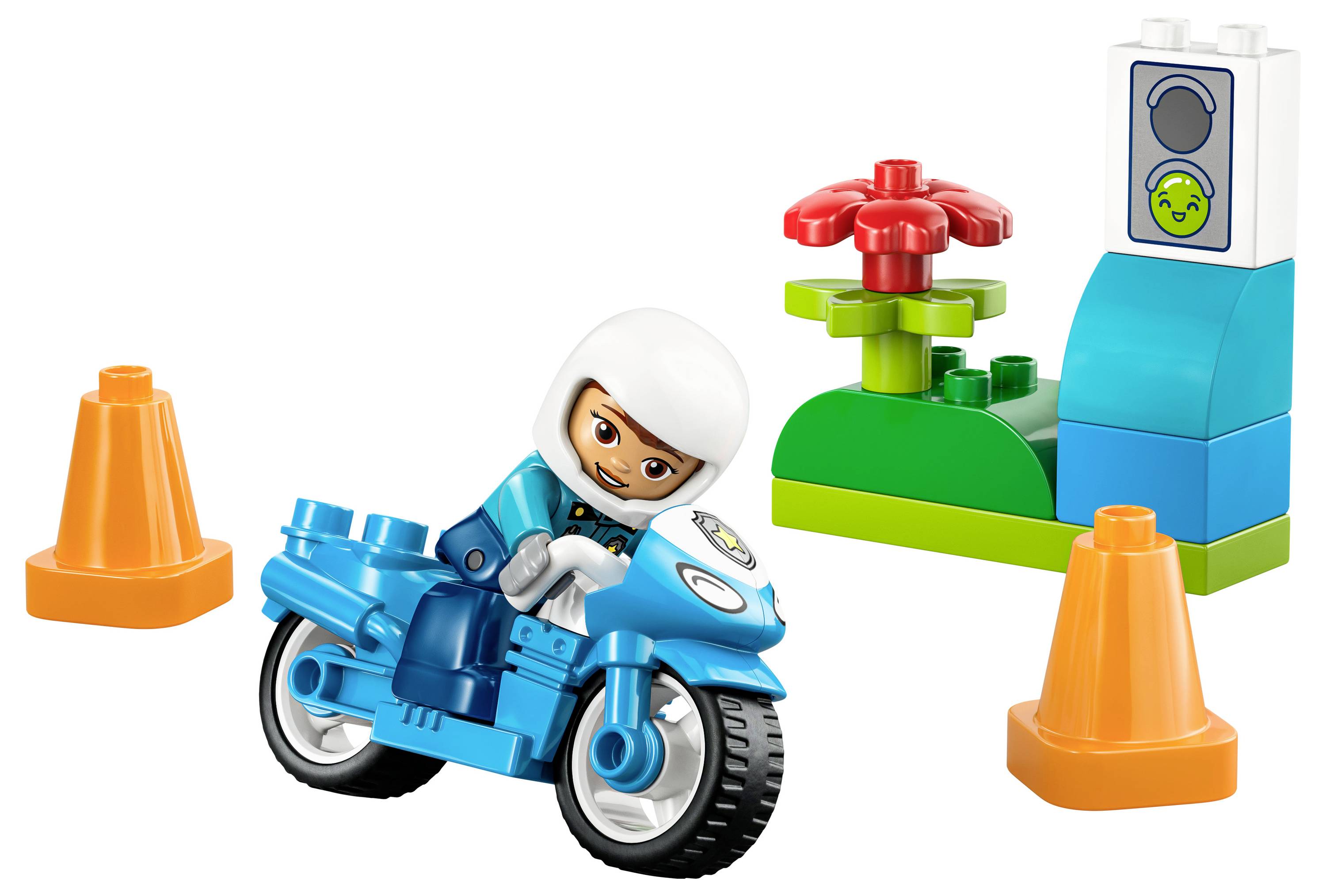 Eine Spielfigur auf einem blauen Motorrad zwischen zwei orangefarbenen Leitkegeln und einer bunten Bauklotzkonstruktion mit einer roten Blume und einem Kontrollpanel.