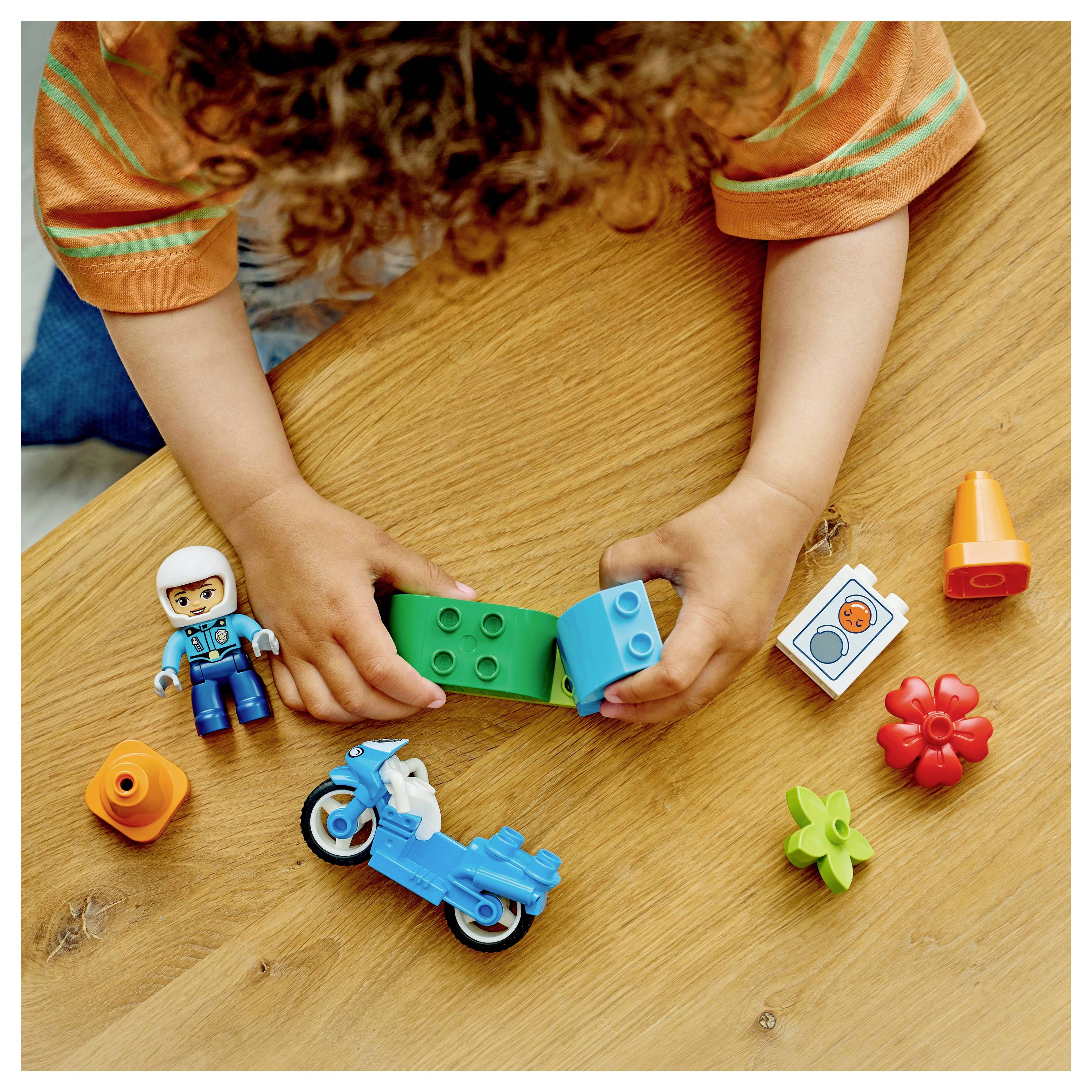 Ein Kind, das mit bunten Spielbausteinen auf einem Tisch baut und dabei eine Miniaturfigur, ein Motorrad und verschiedene Formen verwendet.