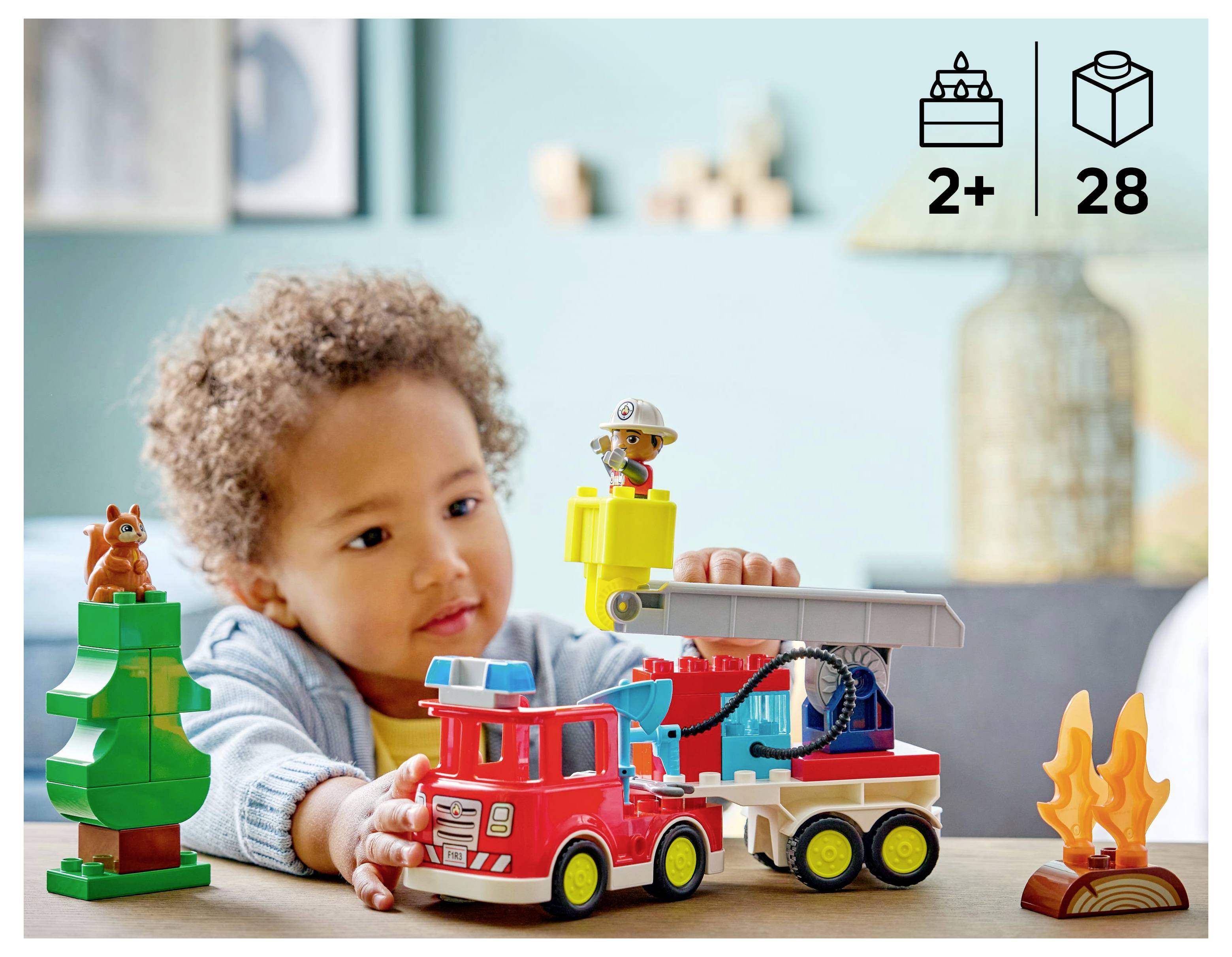 Ein Kind spielt mit einem Spielzeug-Feuerwehr-Set, das einen Baum, eine Feuerwehrmann-Figur und Flammen umfasst, geeignet für Kinder ab 2 Jahren mit insgesamt 28 Teilen.