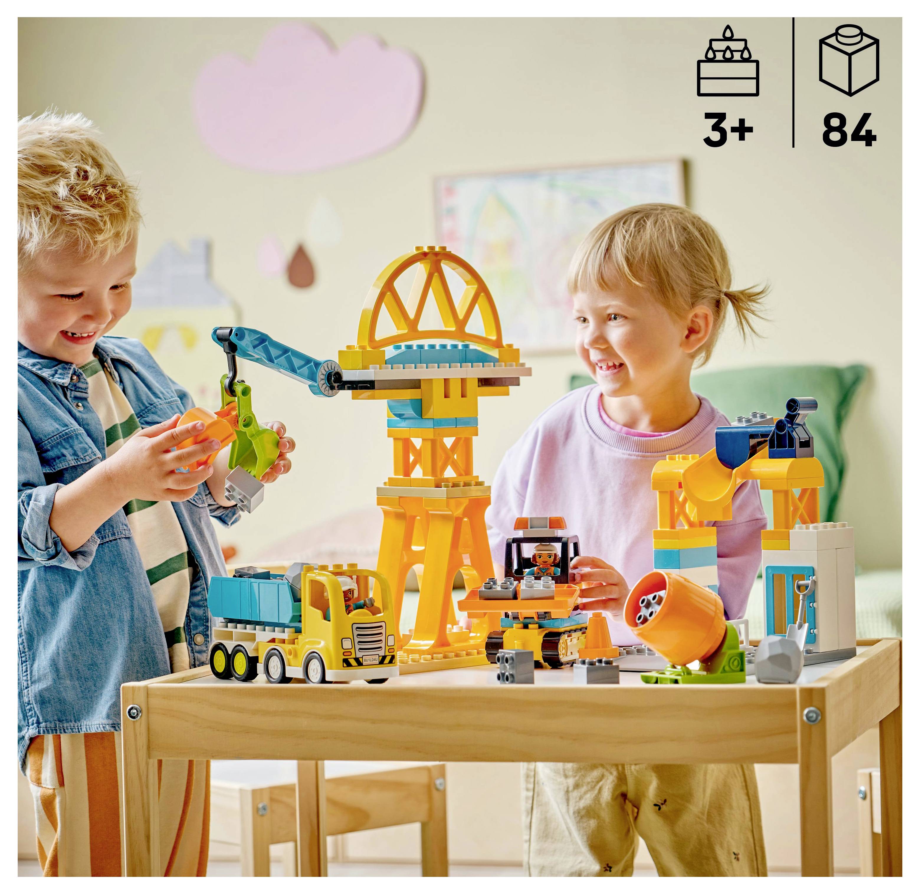 Kinder spielen mit einem bunten Konstruktionsspielzeug-Set, das einen Kran und einen Lastwagen enthält. Geeignet für Kinder ab 3 Jahren, enthält 84 Teile.