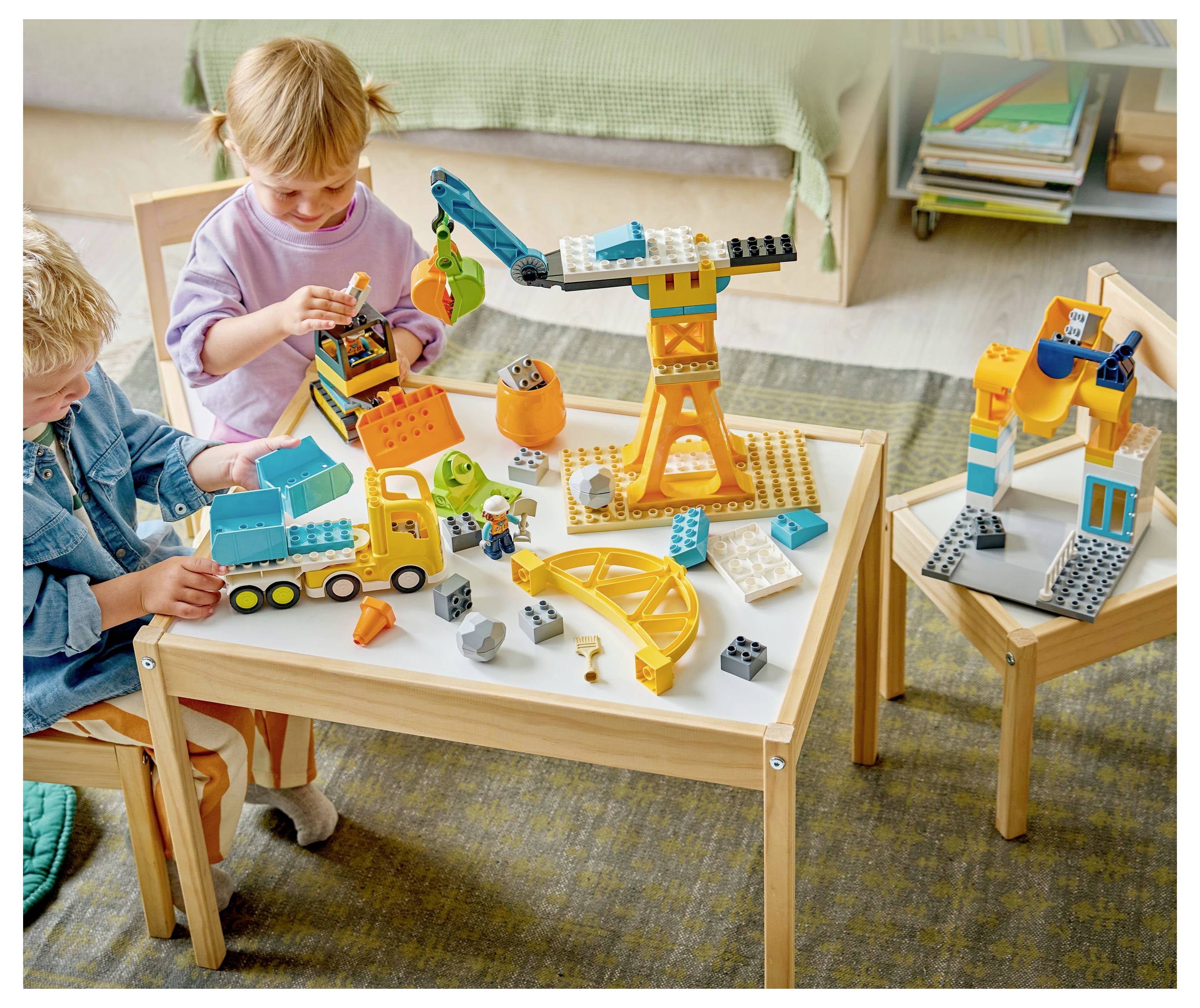 Kinder, die an einem kleinen Tisch mit bunten Bauklötzen spielen und eine Szene mit einem Kran und anderen Fahrzeugen konstruieren.