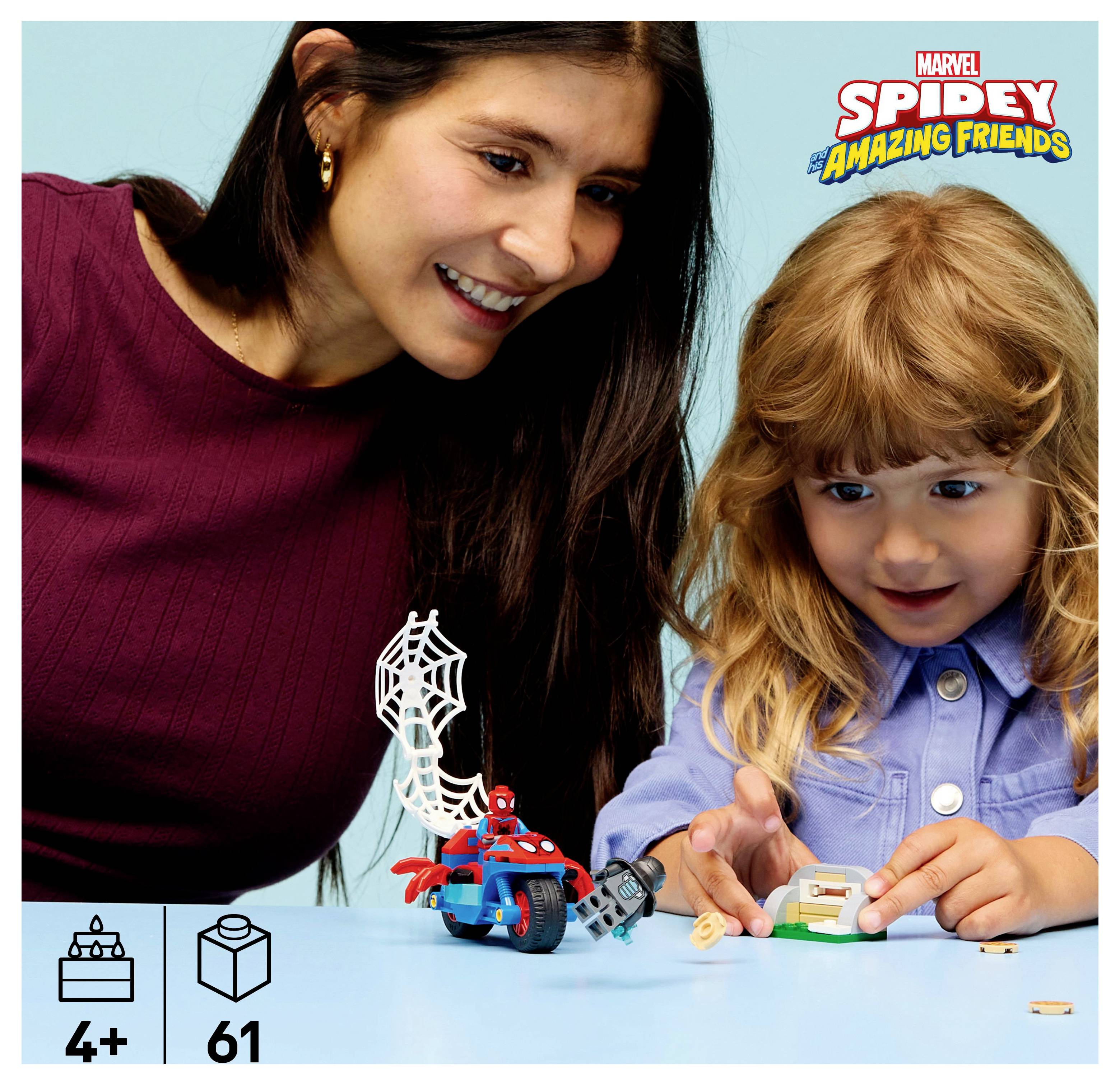 Eine Frau und ein Kind spielen mit einem Spielzeug, das einen kleinen roten und blauen Superhelden auf einem netzförmigen Stück zeigt, zusammen mit Bauklötzen und Blöcken, die mit '4+' und '61' beschriftet sind.