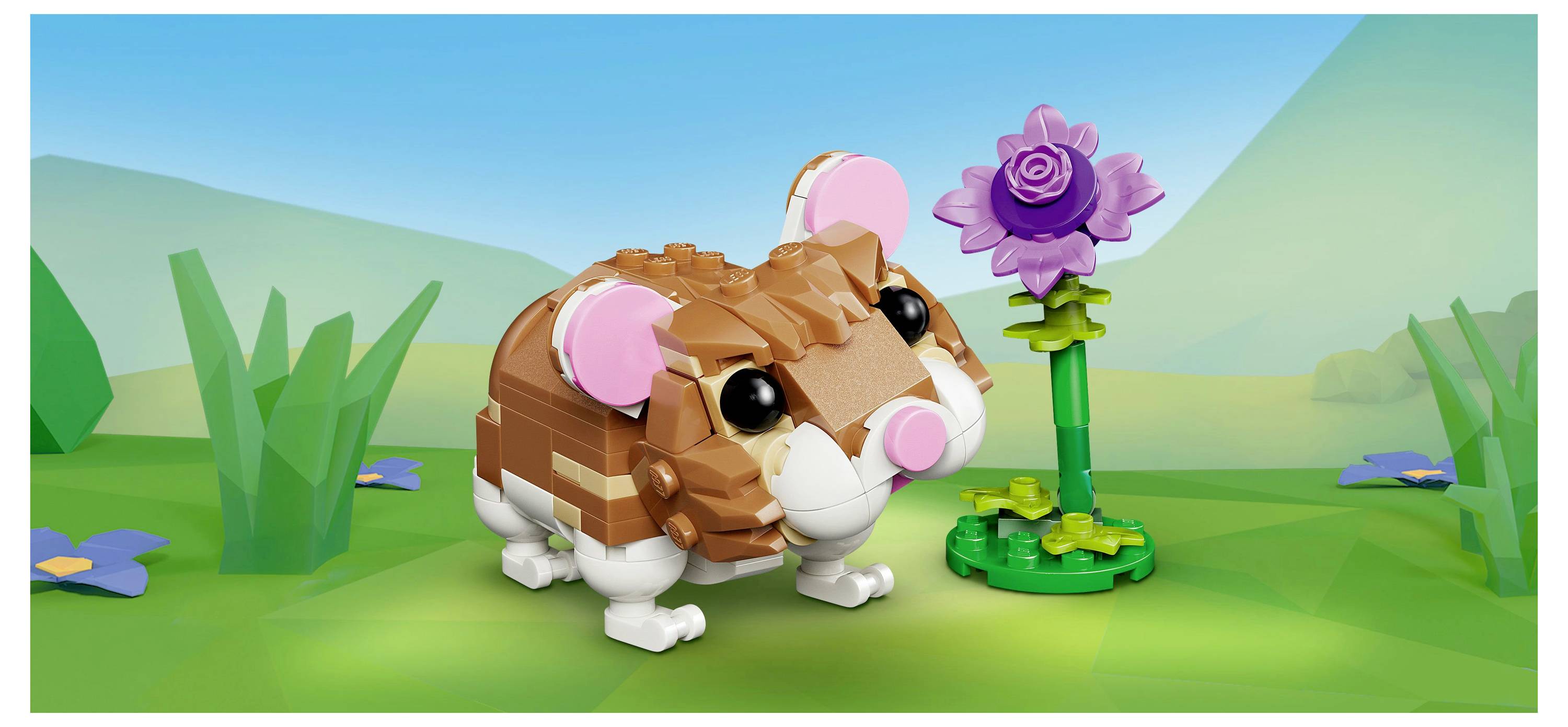 Ein kleiner LEGO-Hamster steht auf grünem Gras mit einer lila Blume daneben. Der Hintergrund zeigt eine Graslandschaft unter einem blauen Himmel.