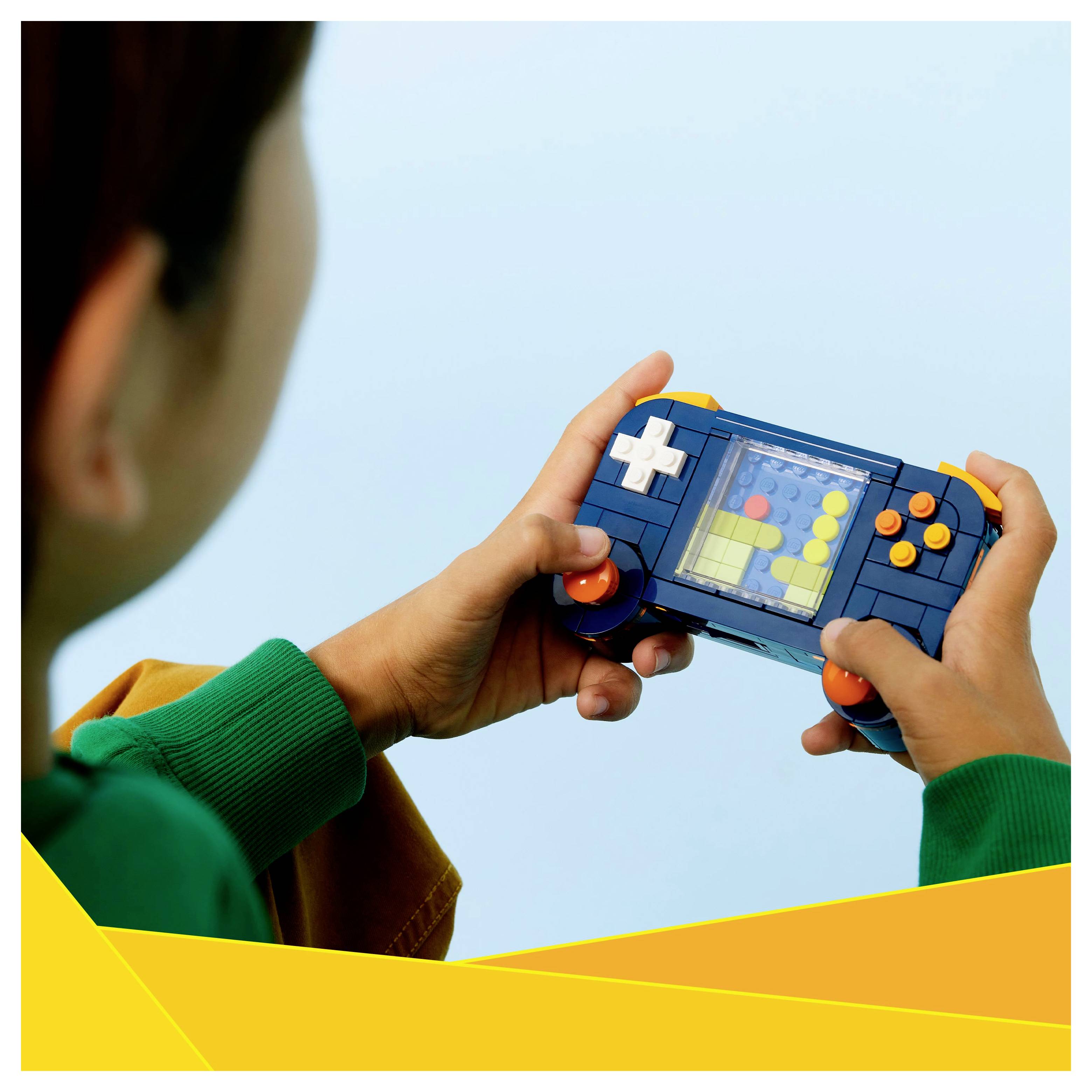 Eine Person hält ein farbenfrohes, spielzeughaftes tragbares Spielgerät mit sichtbaren roten, weißen und gelben Tasten in einem hell beleuchteten Raum.