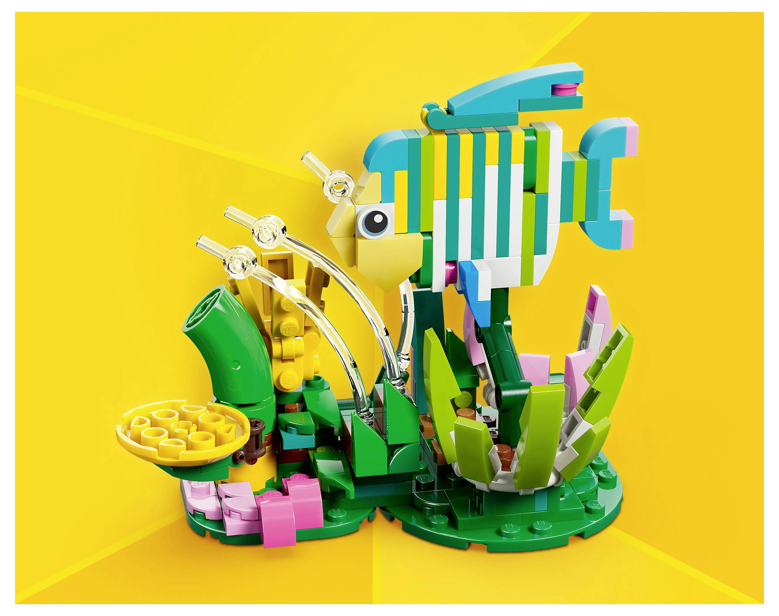 Eine bunte LEGO-Fischdisplay mit einem lebhaften gelben Hintergrund, die einen Fisch zwischen grünen und rosa LEGO-Pflanzen und dekorativen Elementen zeigt.