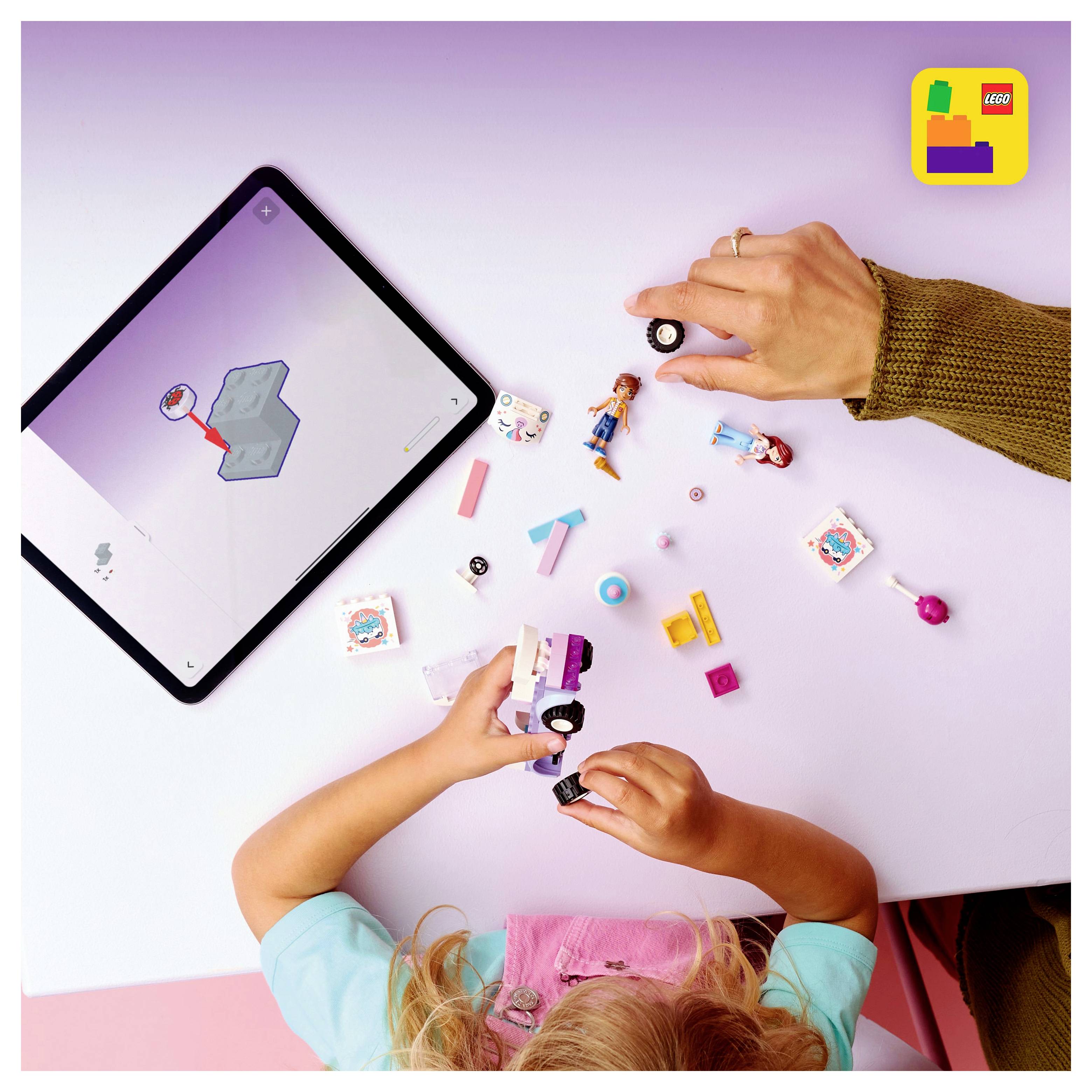 Ein Kind, das an einem rosa Tisch mit einem LEGO-Set spielt und ein Fahrzeug zusammenbaut, während es Anweisungen auf dem Bildschirm eines Tablets daneben verfolgt.