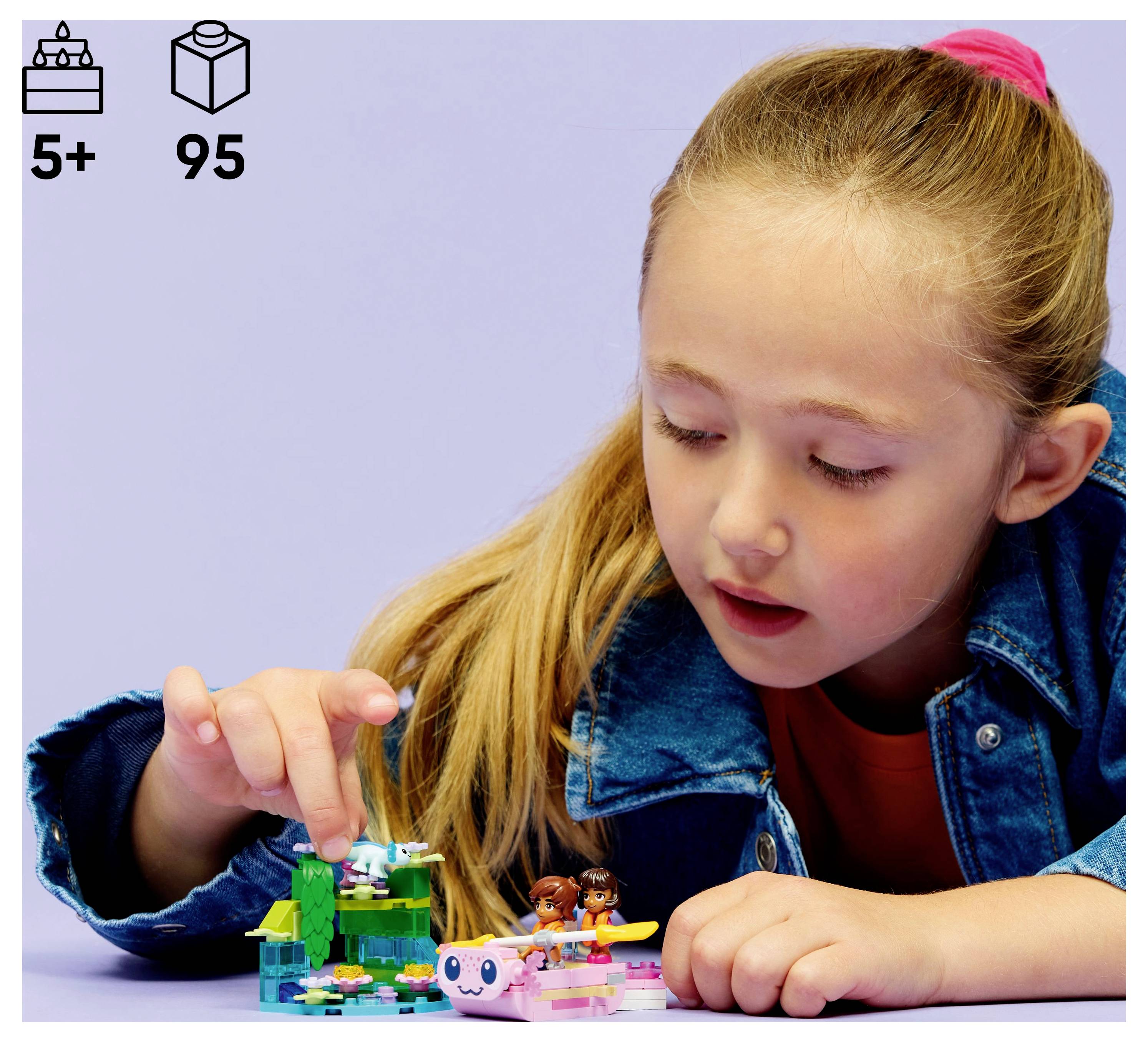 Ein Kind spielt mit einem kleinen, bunten Bausteinset auf einem Tisch, das ein Modell mit Bäumen und Figuren darstellt. Die Schachtel empfiehlt das Spielzeug ab 5 Jahren, mit 95 Teilen.