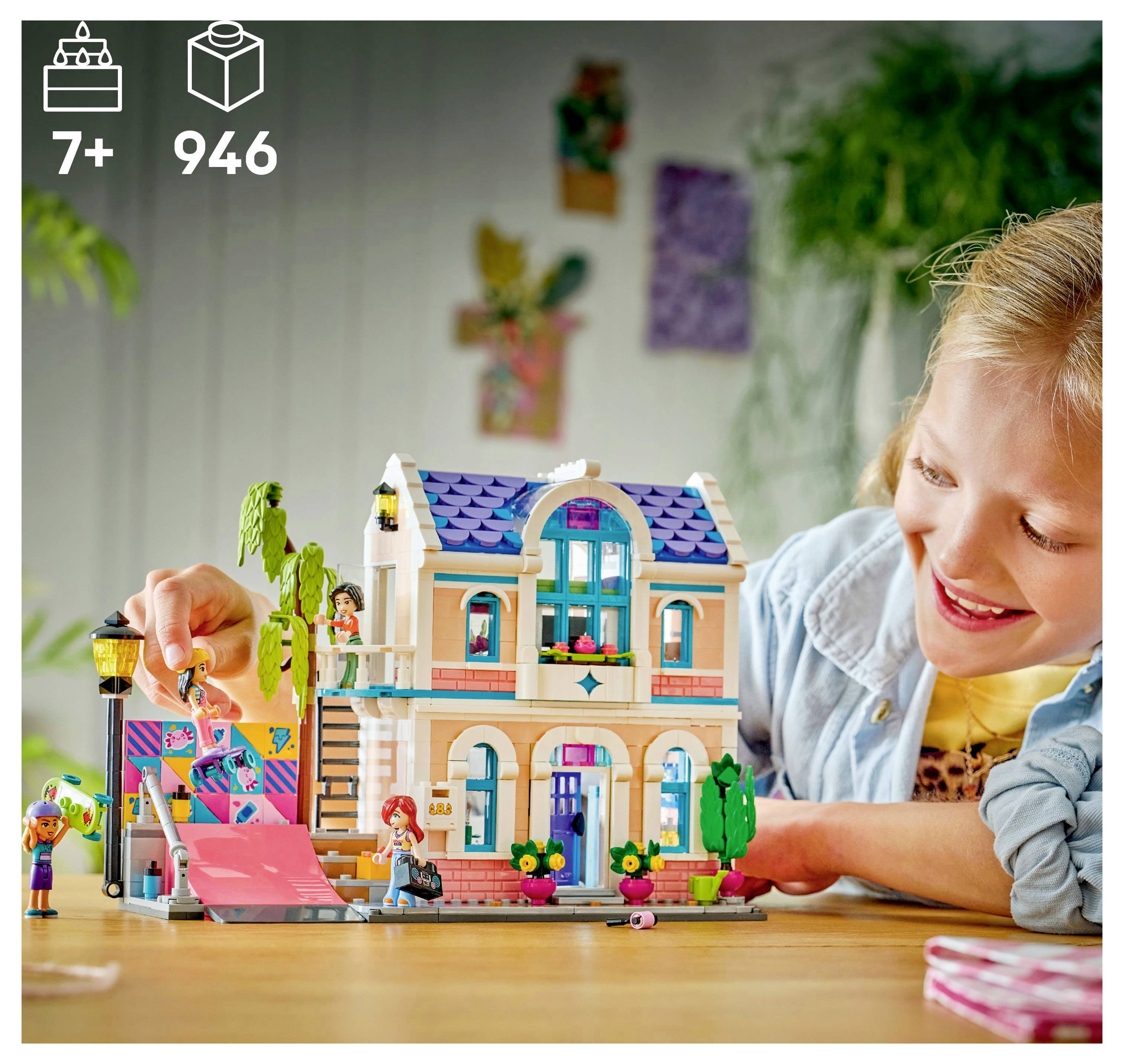 Ein Kind spielt fröhlich mit einem zweistöckigen Spielgebäude-Set, das eine rosa Rampe und kleine Figuren enthält und für Kinder ab 7 Jahren geeignet ist, mit insgesamt 946 Teilen.