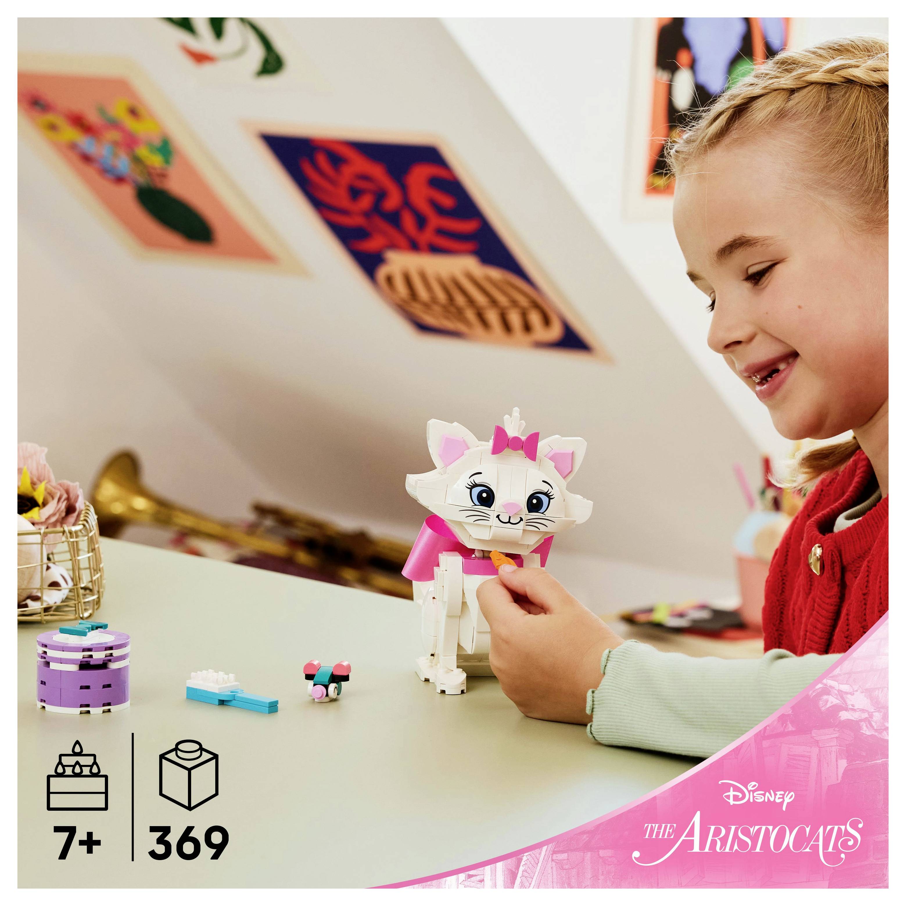 Ein Kind baut eine kleine Katzenfigur aus LEGO-Teilen an einem Tisch, mit einem dekorierten Zimmer im Hintergrund. Der Text zeigt '7+ 369'.