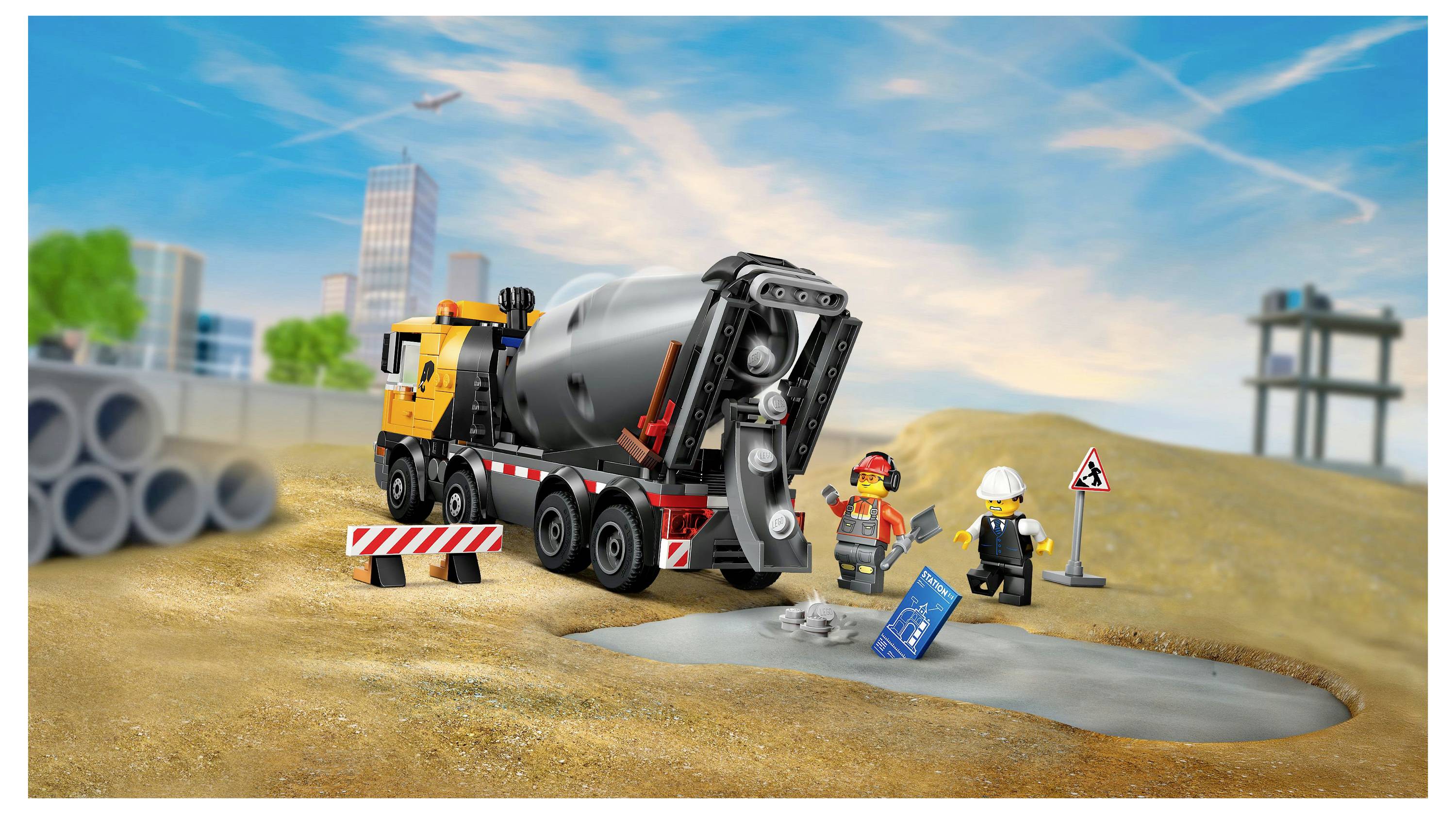 Ein Spielzeug-Betonmischer auf einer Baustelle mit zwei Spielzeugarbeitern. Ein Arbeiter hält einen Bauplan. Verschiedene Bauelemente sind zu sehen.