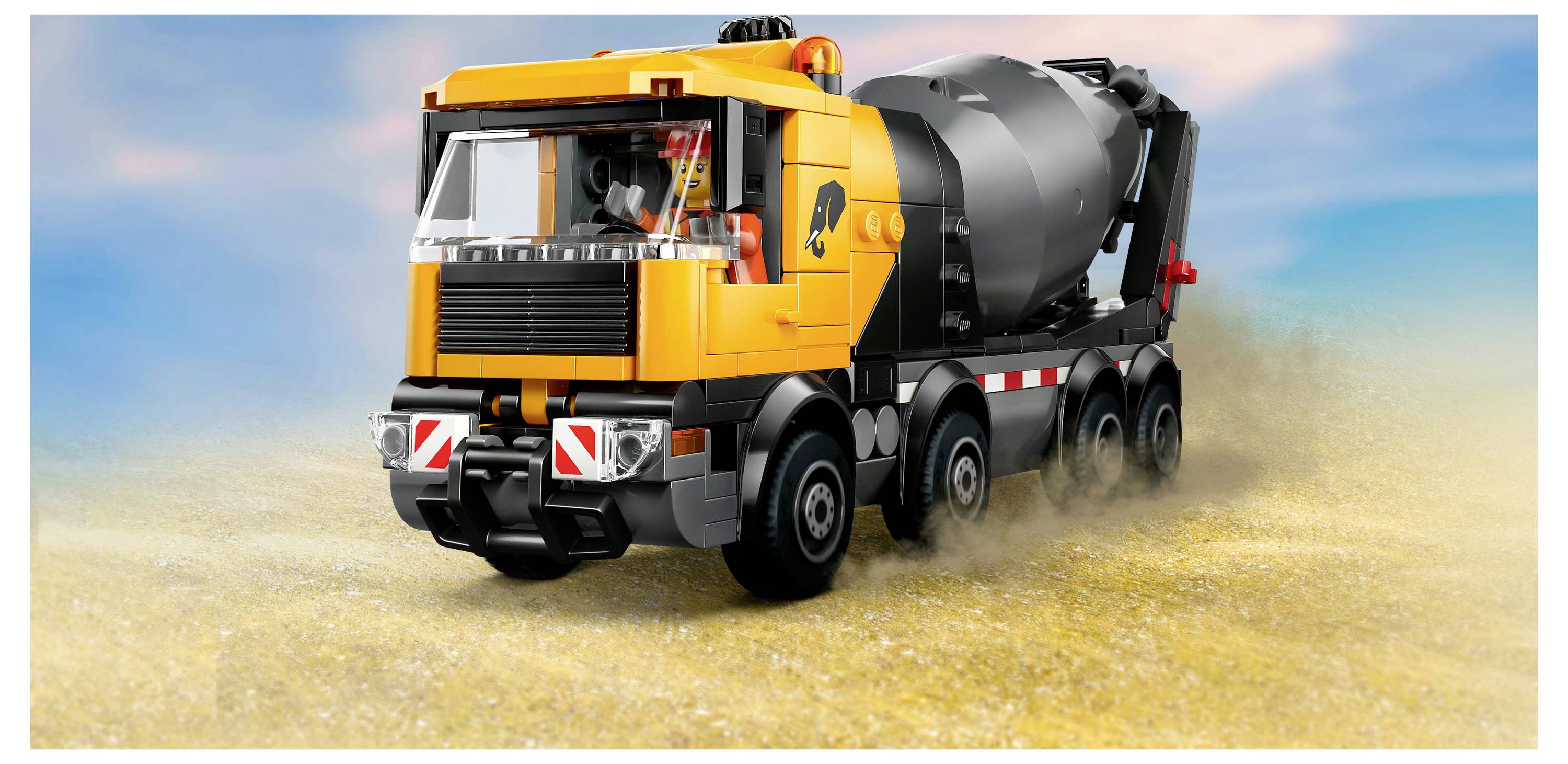 Ein gelb-schwarzer Spielzeug-Betonmischer auf einer sandigen Oberfläche vor einem klaren Himmelshintergrund.