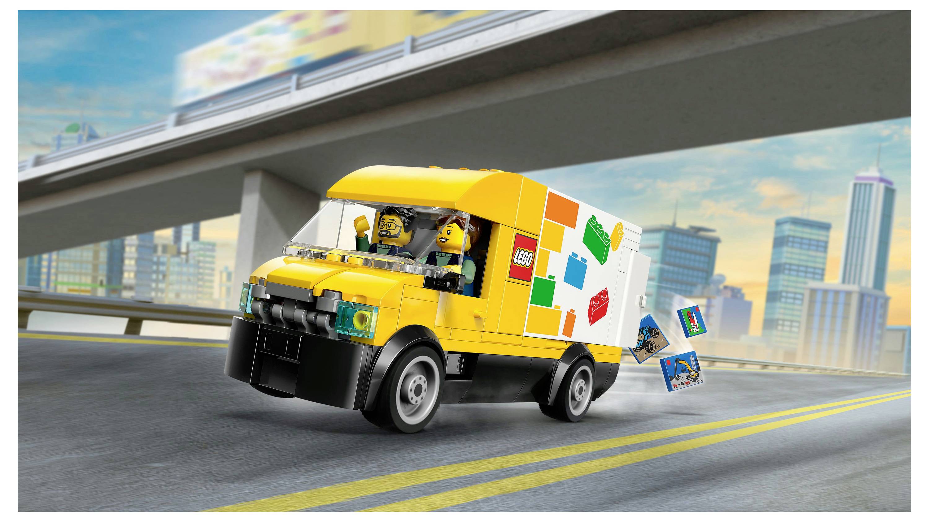 Ein gelber Spielzeug-Lieferwagen, der auf einer Autobahn fährt, mit LEGO-Figuren im Inneren und einer Stadtkulisse im Hintergrund. Der Lastwagen hat LEGO-Steine an seiner Seite.